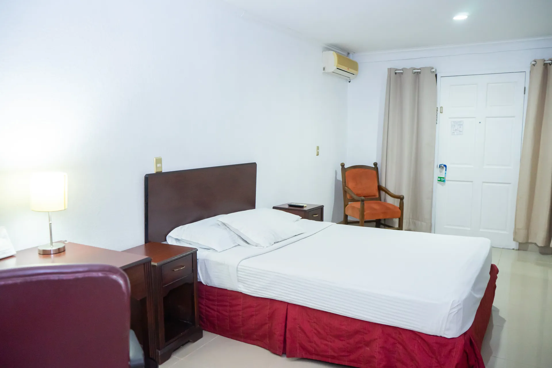 Habitación de hotel con cama, silla, escritorio y paredes blancas.