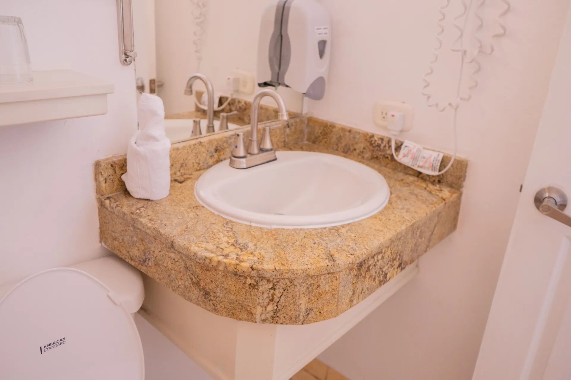 Lavabo de baño con encimera de granito y espejo, junto a un inodoro.