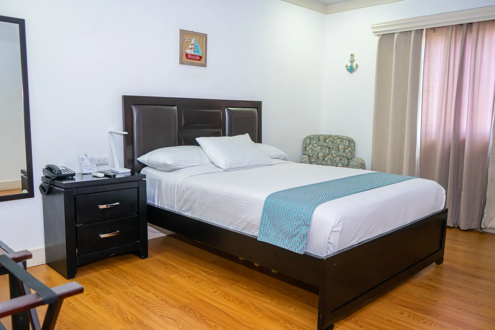 Dormitorio con cama, mesita de noche, sillón, cortinas y espejo.