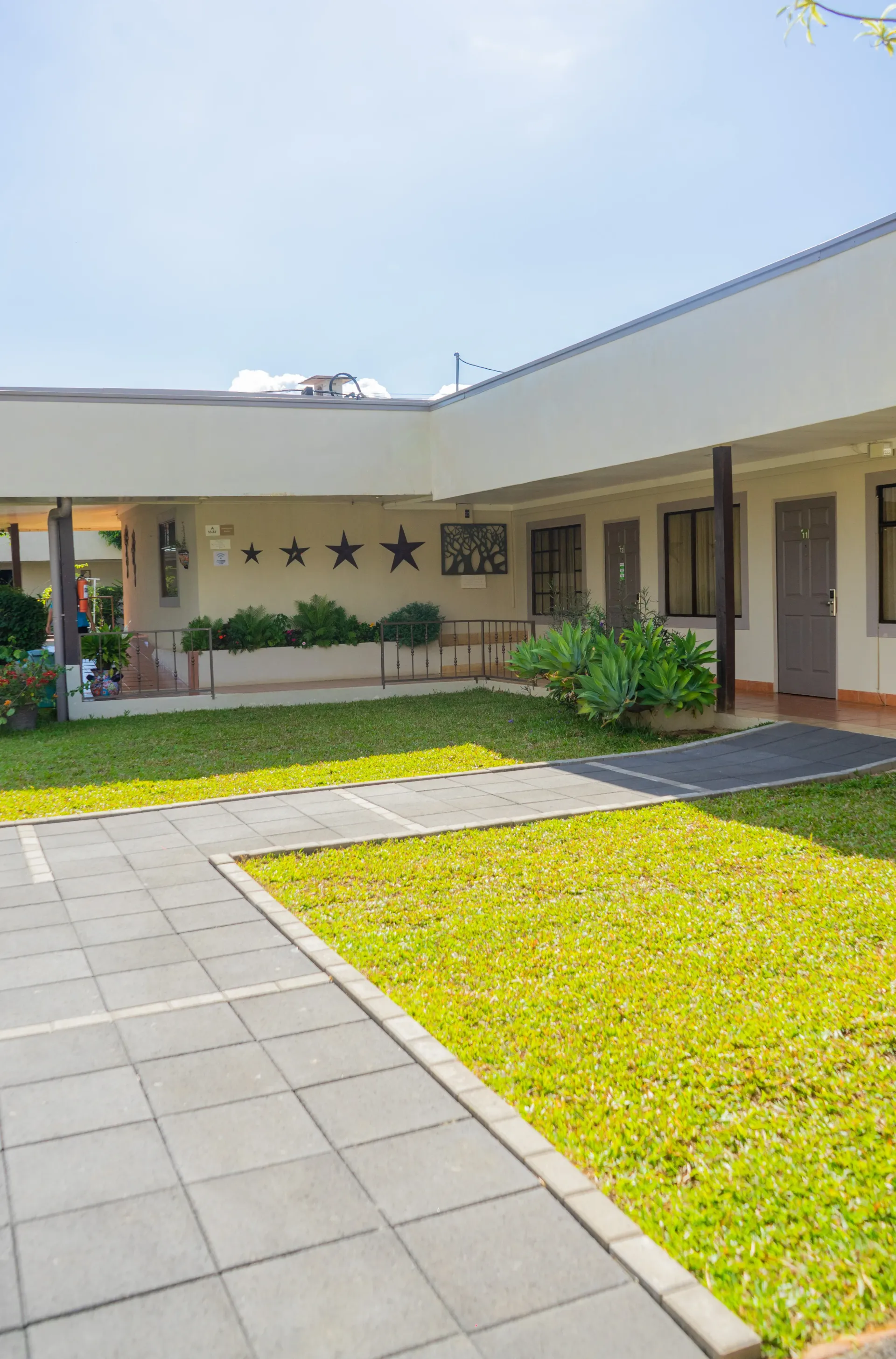 Patio con césped verde, pasarela y edificios de colores claros bajo un cielo azul.