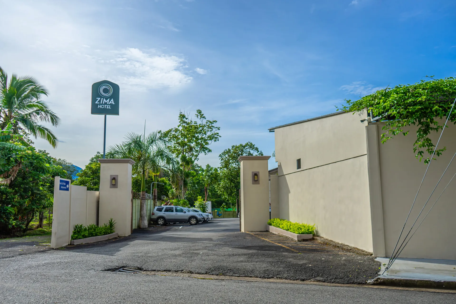 Entrada de un hotel, entrada de piedra gris, paredes color crema, letrero. Cielo azul.