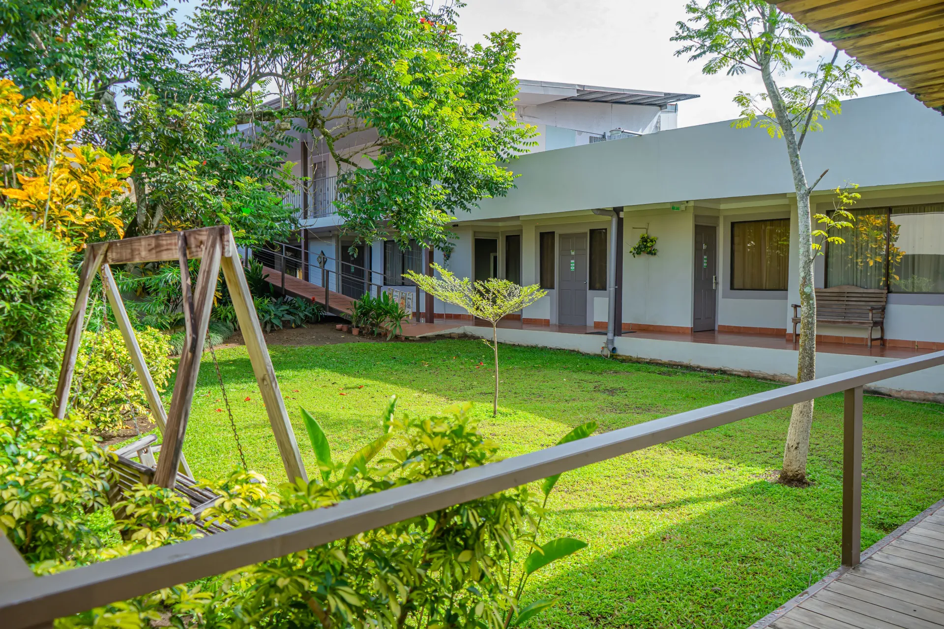 Patio verde con césped, árboles, un columpio y un edificio con puertas y ventanas.