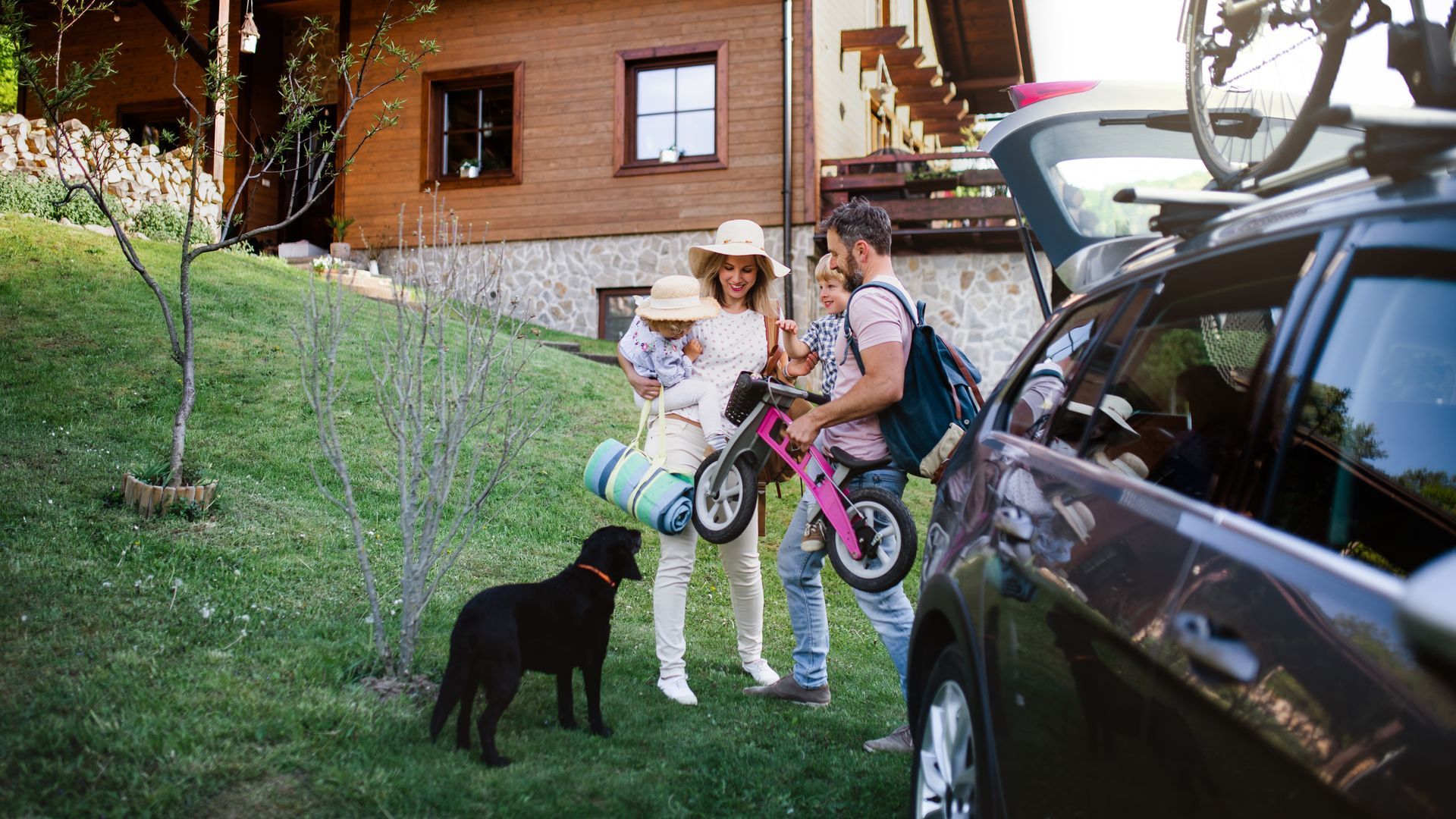 A family and a dog are standing next to a car.
