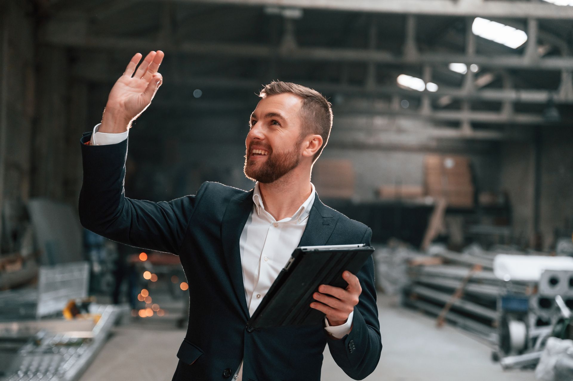 A man in a suit is holding a tablet in a warehouse.