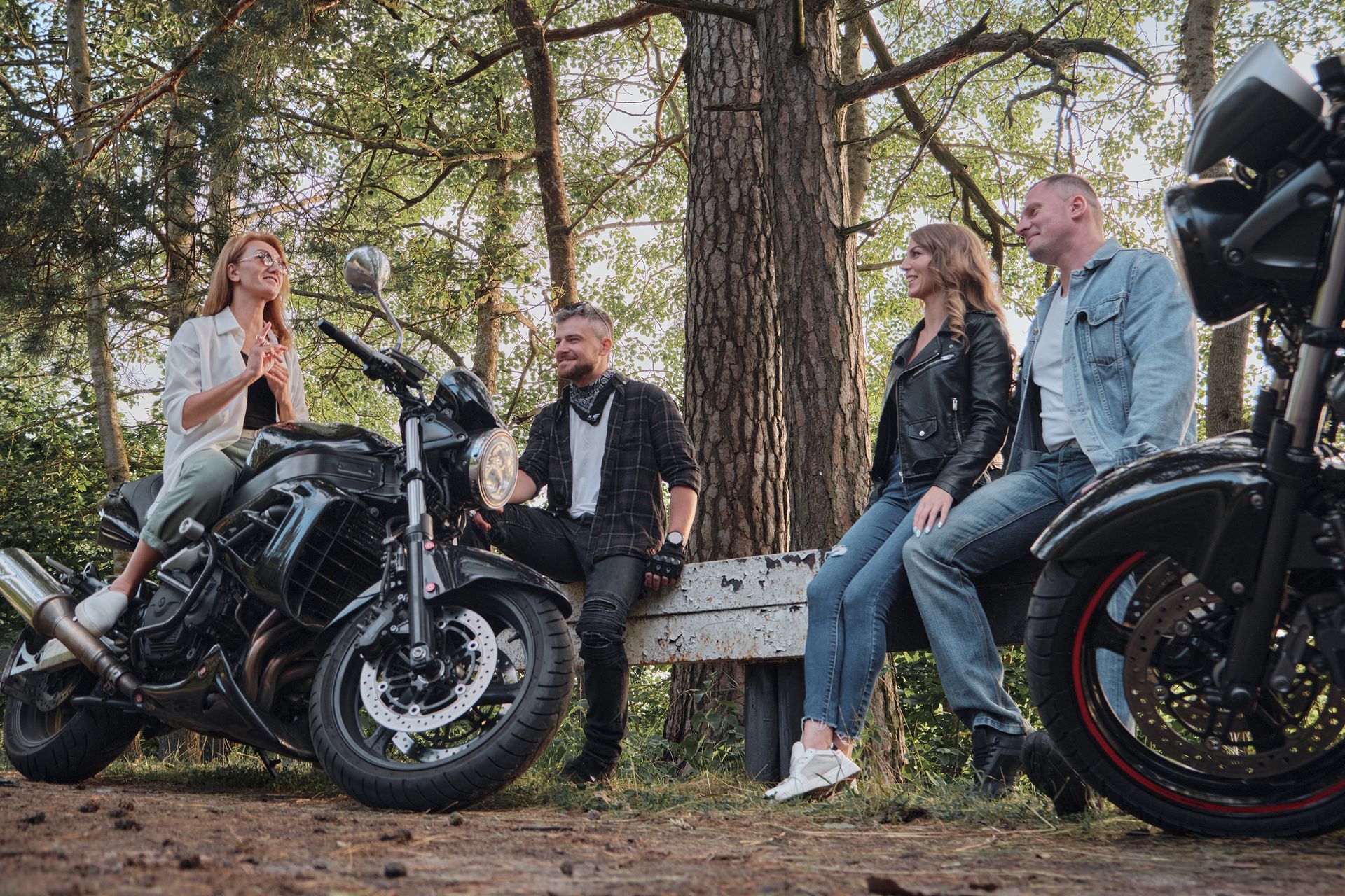 A group of people are sitting on a bench next to motorcycles.