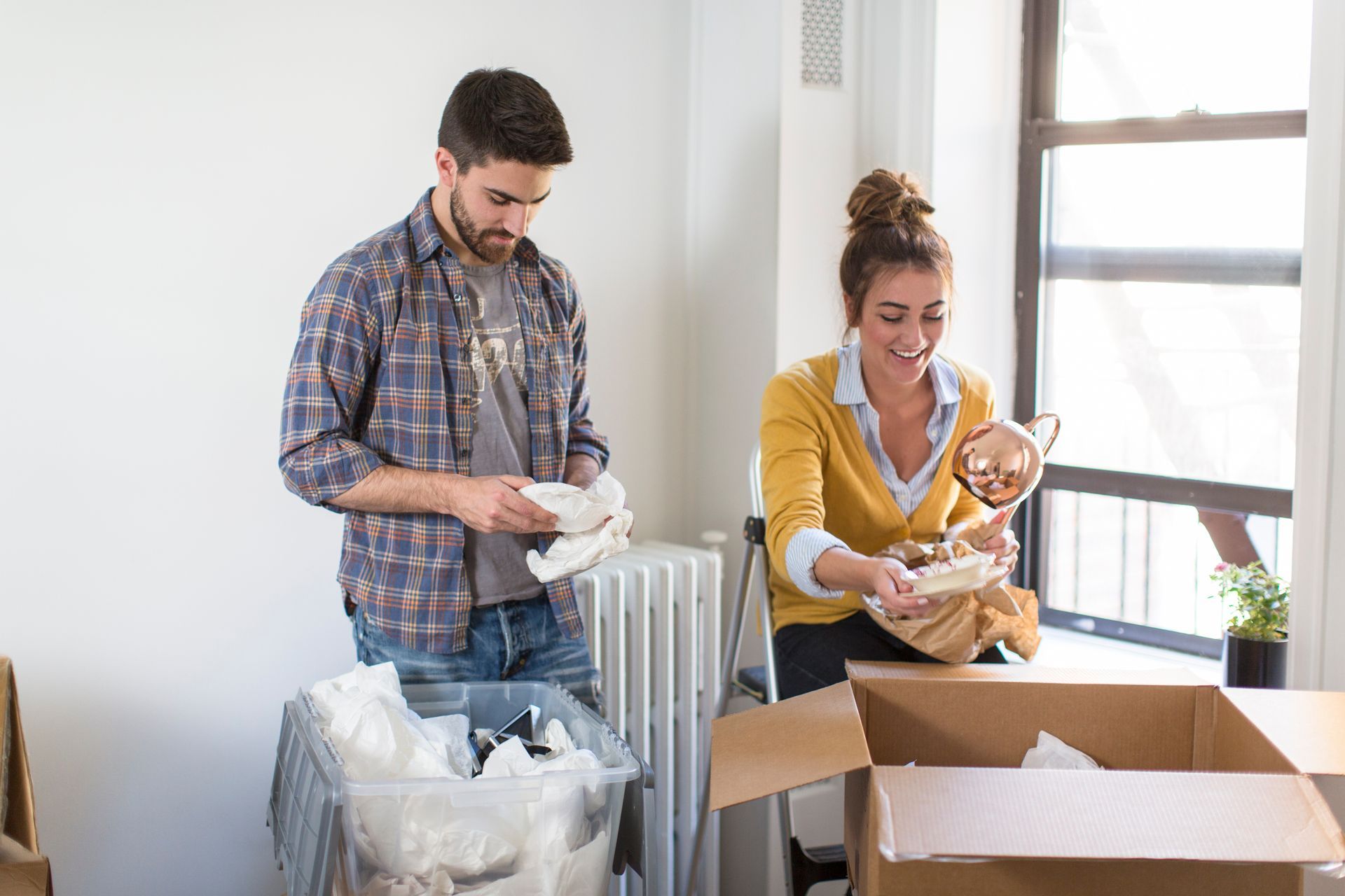 A man and a woman are packing boxes in a room.