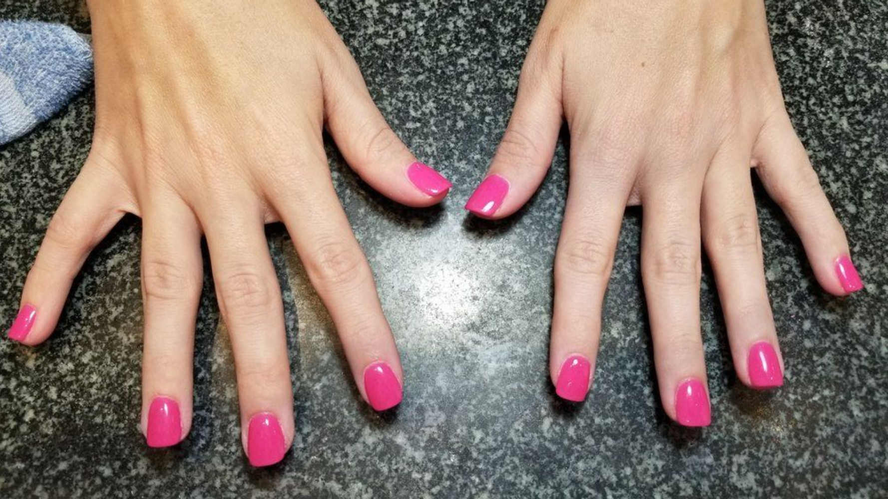 Hands with pink nail polish on a dark speckled surface.