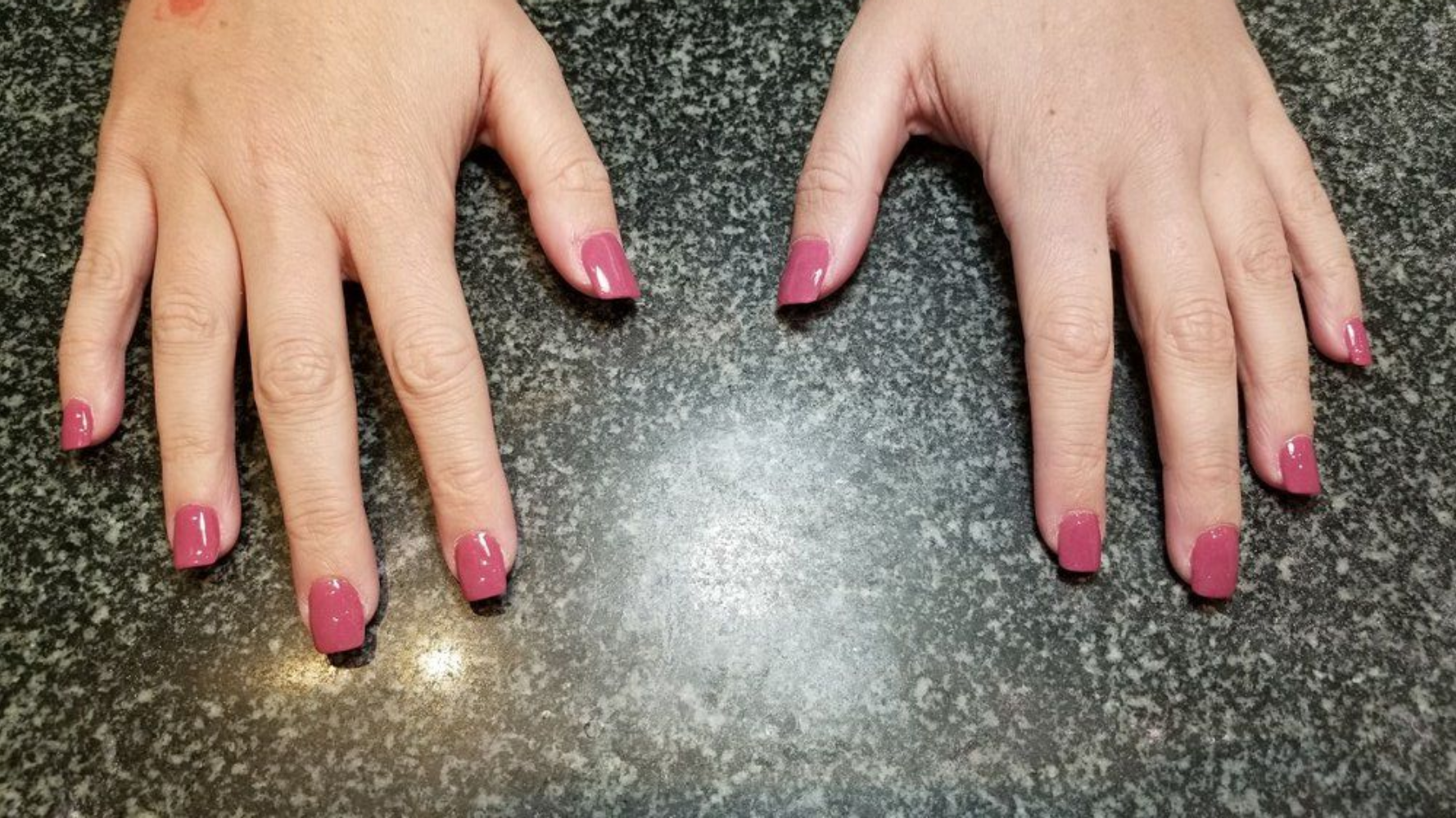 Two hands with pink nail polish on a speckled countertop.