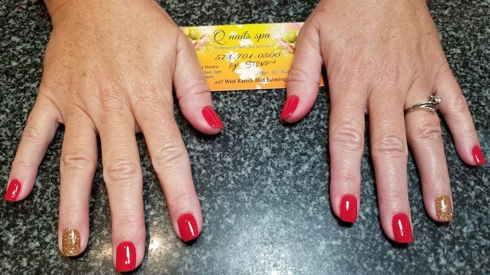 Hands with red nails and one gold nail, on a dark countertop, with a business card between them.