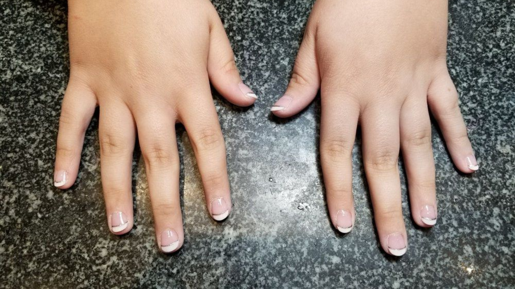 Two hands with French tip manicured nails, resting on a dark countertop.