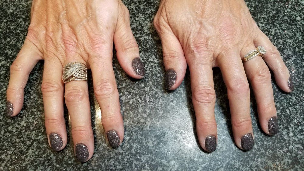 Two hands with dark gray glitter nail polish, rings on fingers.