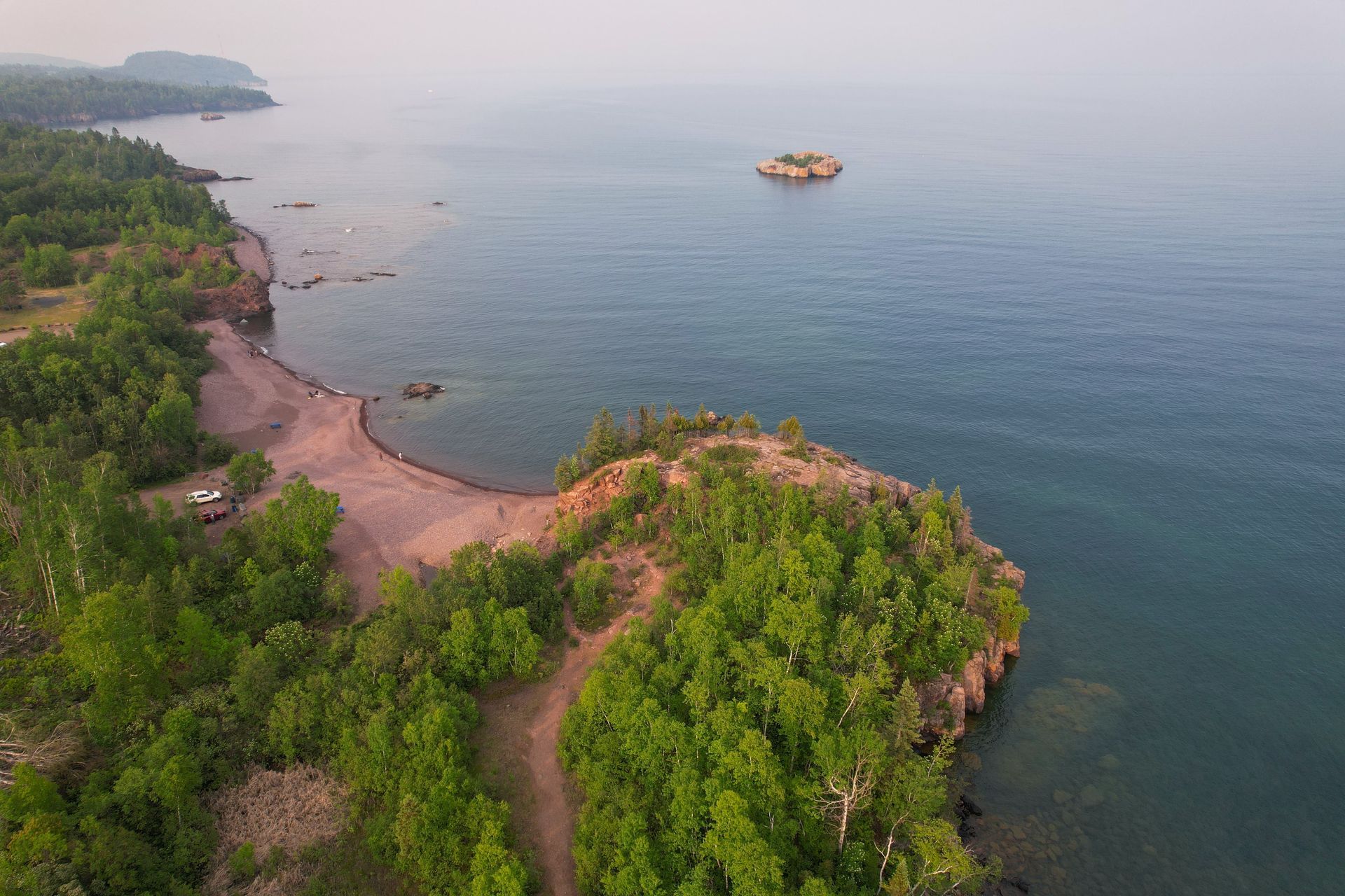 Coastal view with lake, small island, and green trees.