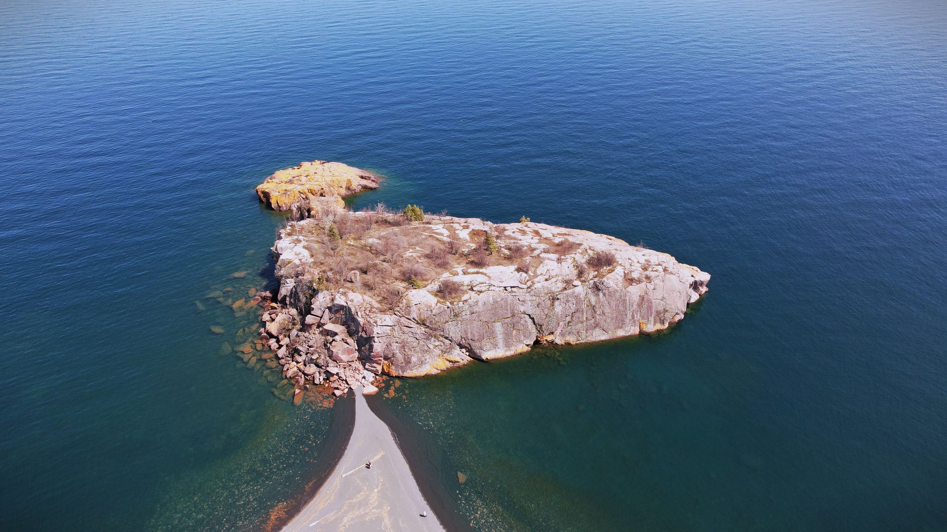 Small rocky island in clear blue water, connected by a narrow stone path.