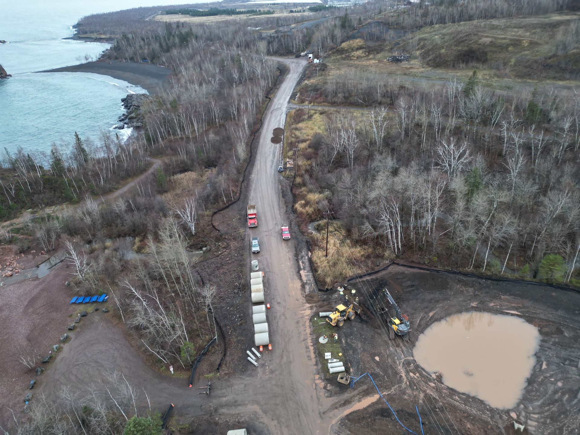 Aerial view of a coastal road with construction activity. Several vehicles and equipment are present.