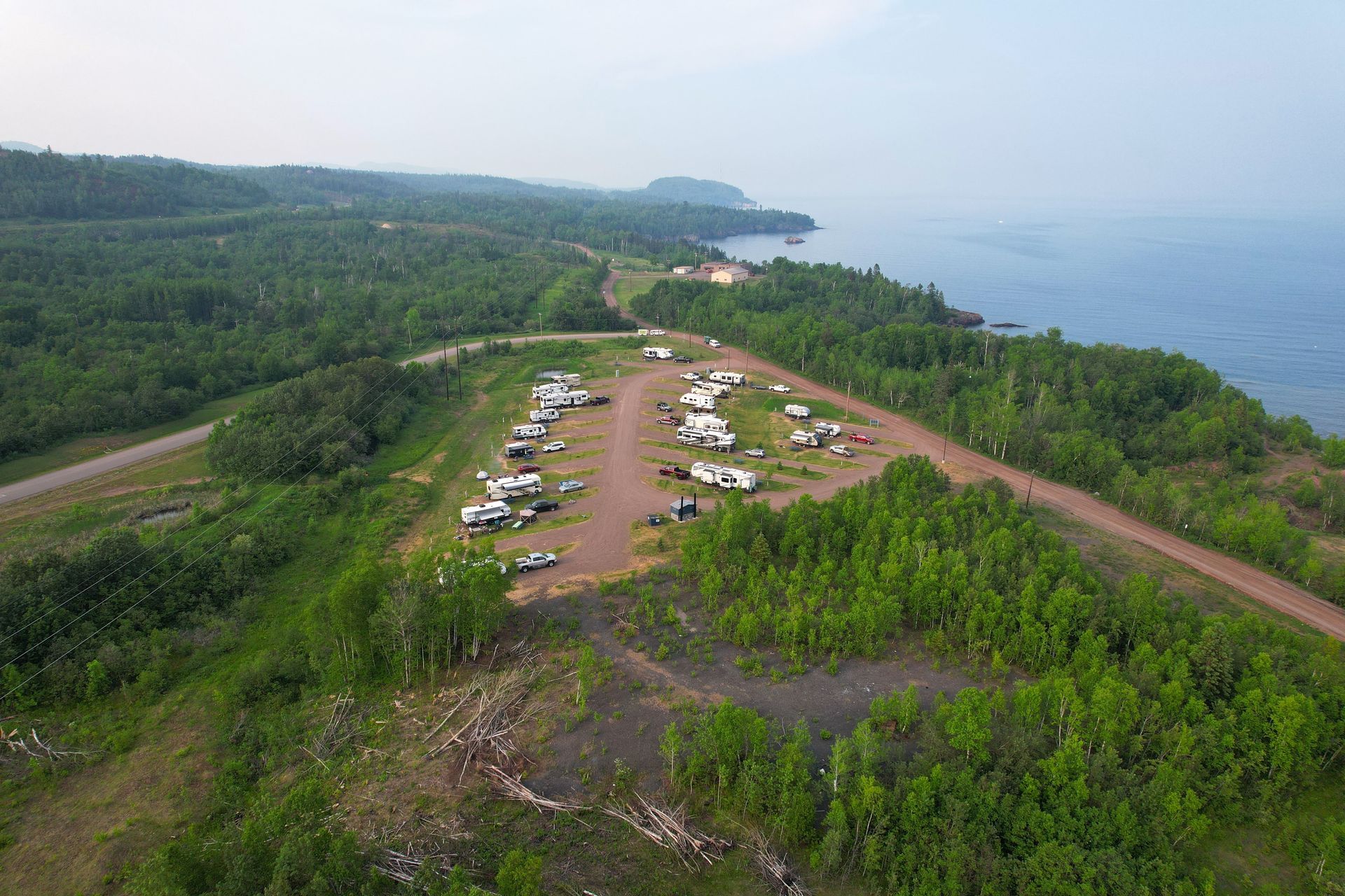 Campground on a grassy hill overlooking a body of water with RVs and trees.
