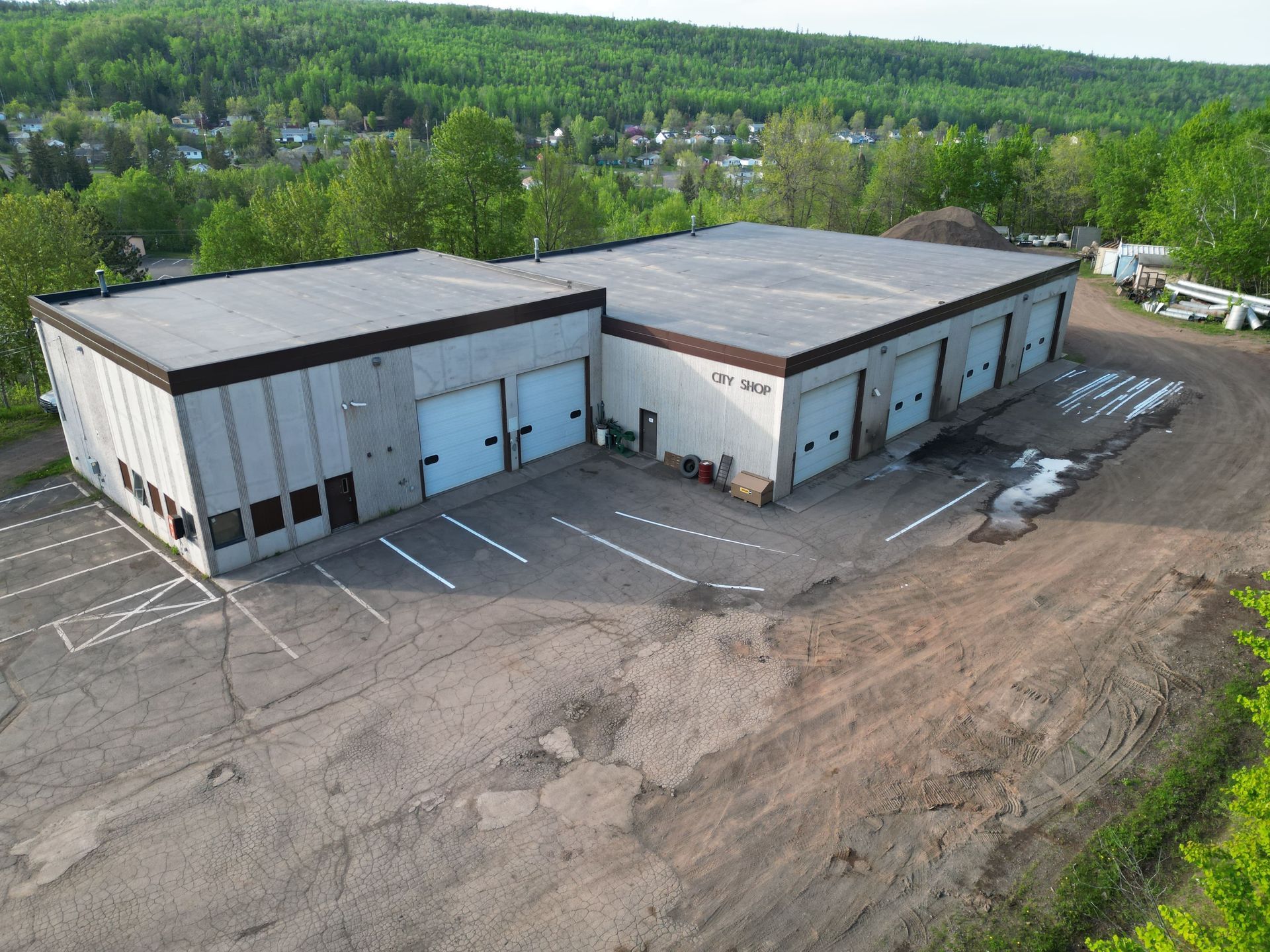 Industrial building with multiple garage doors and parking spaces, located outside, surrounded by trees.