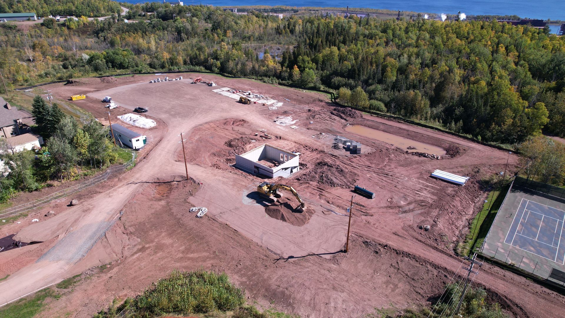 Construction site with buildings under development near tennis courts and trees.