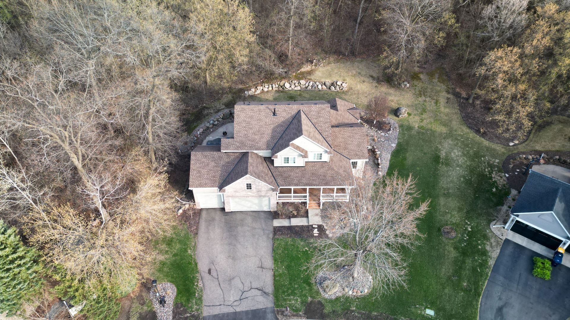Aerial view of a house with a brown roof and a long driveway, surrounded by trees and grass.