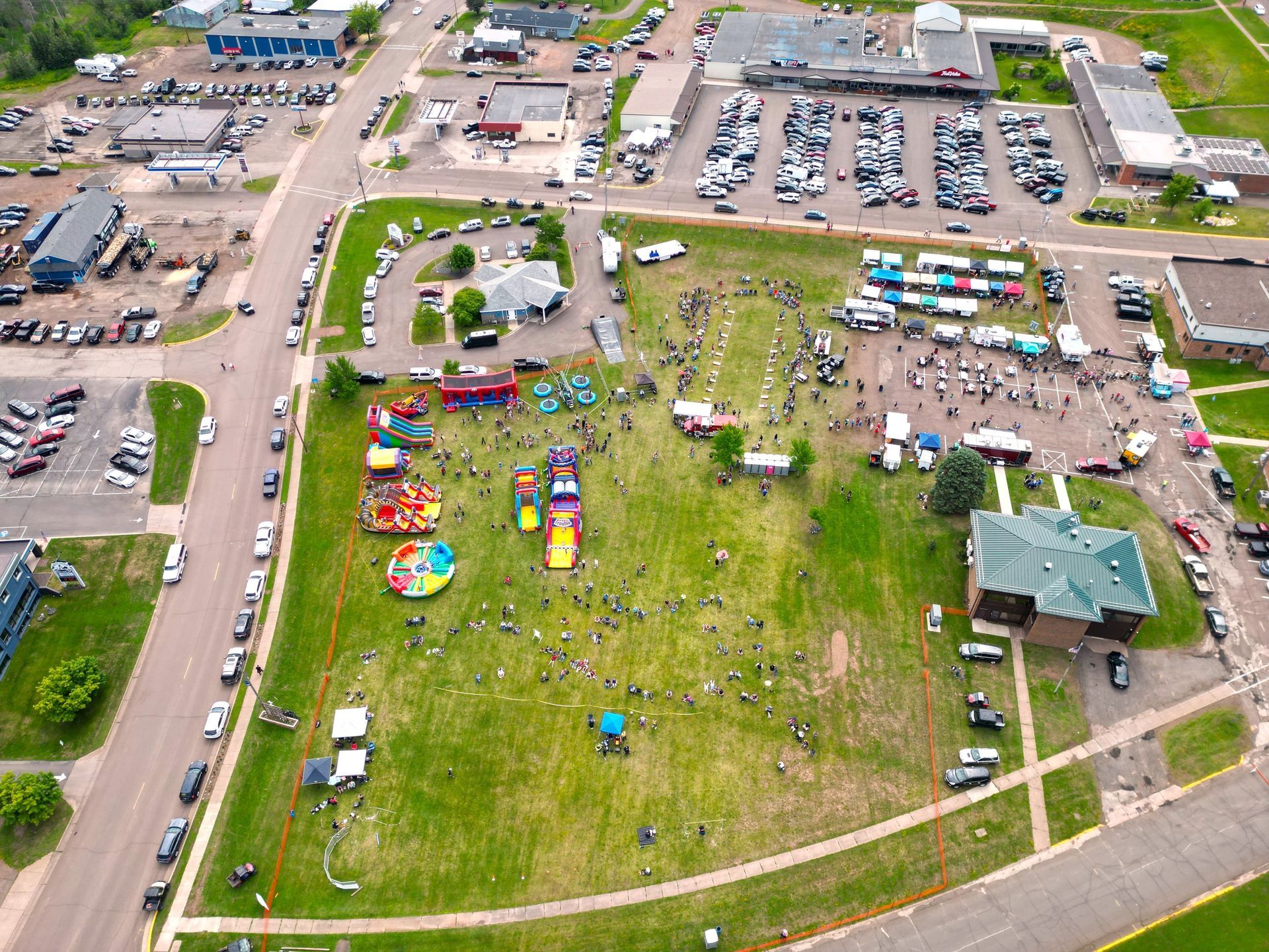 Aerial view of an outdoor event on a grassy field with people, bounce houses, and food trucks.