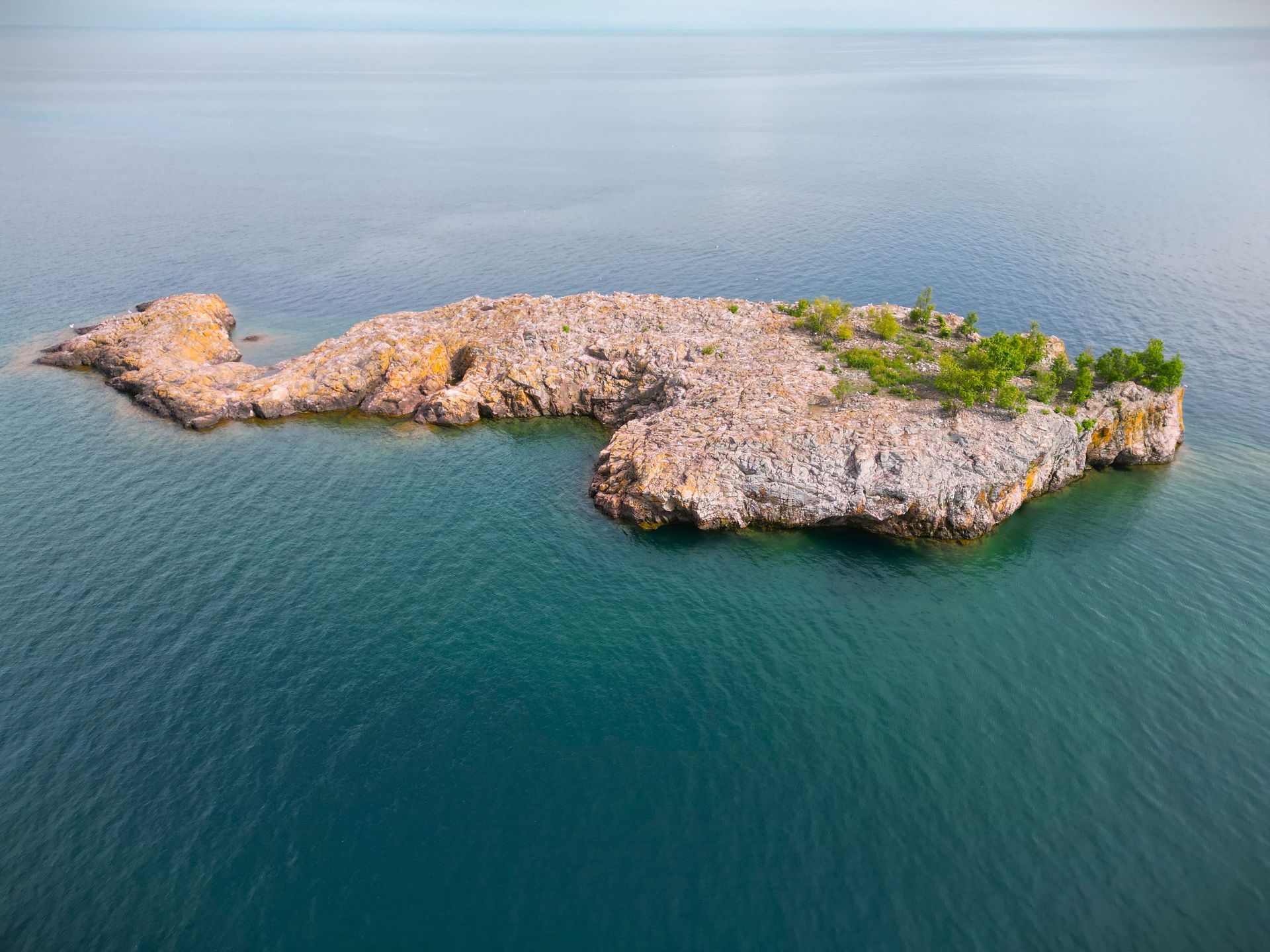 Rocky island in turquoise water, with sparse green vegetation on the top.