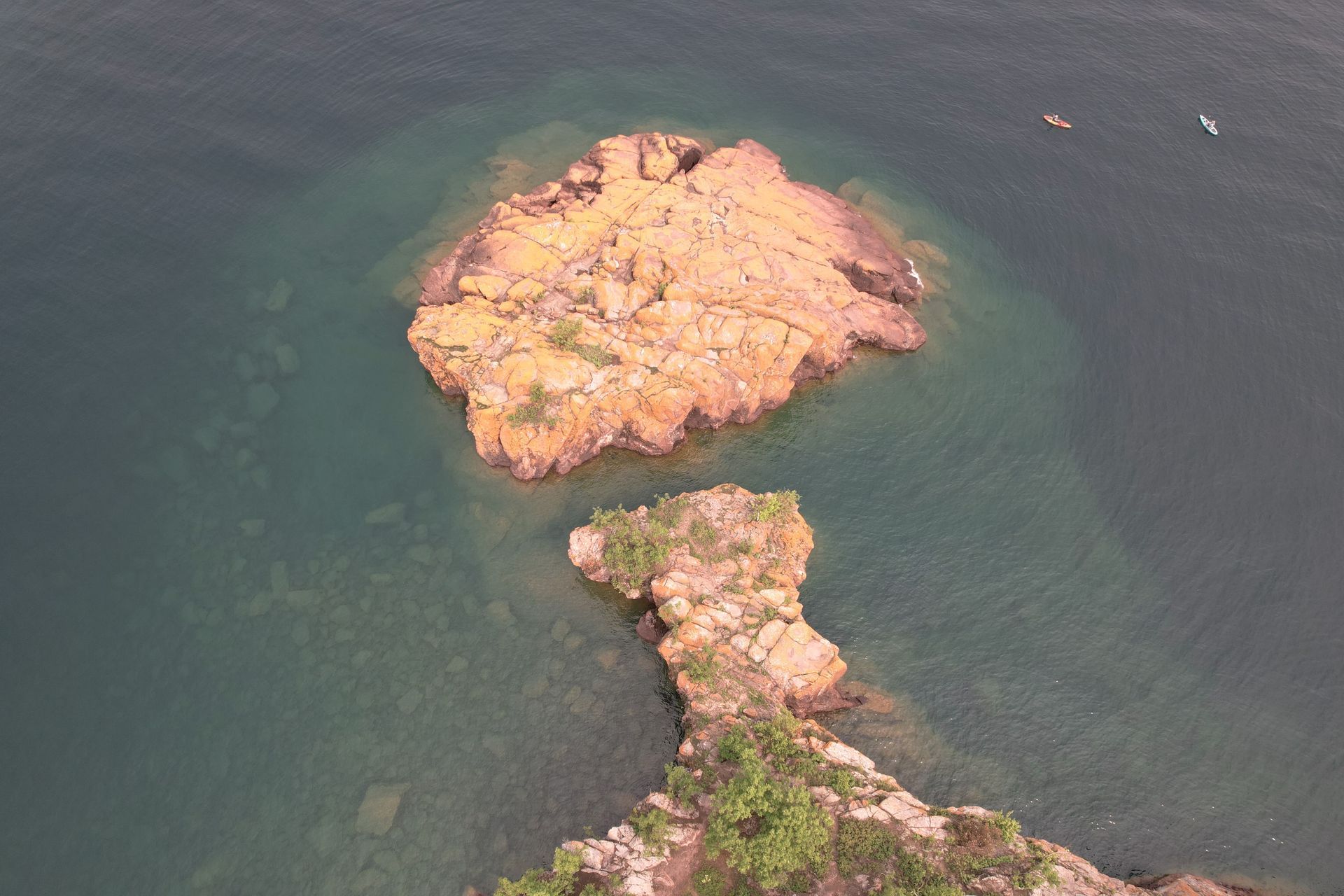 Rocky island formations in clear water. Two kayaks visible in distance.