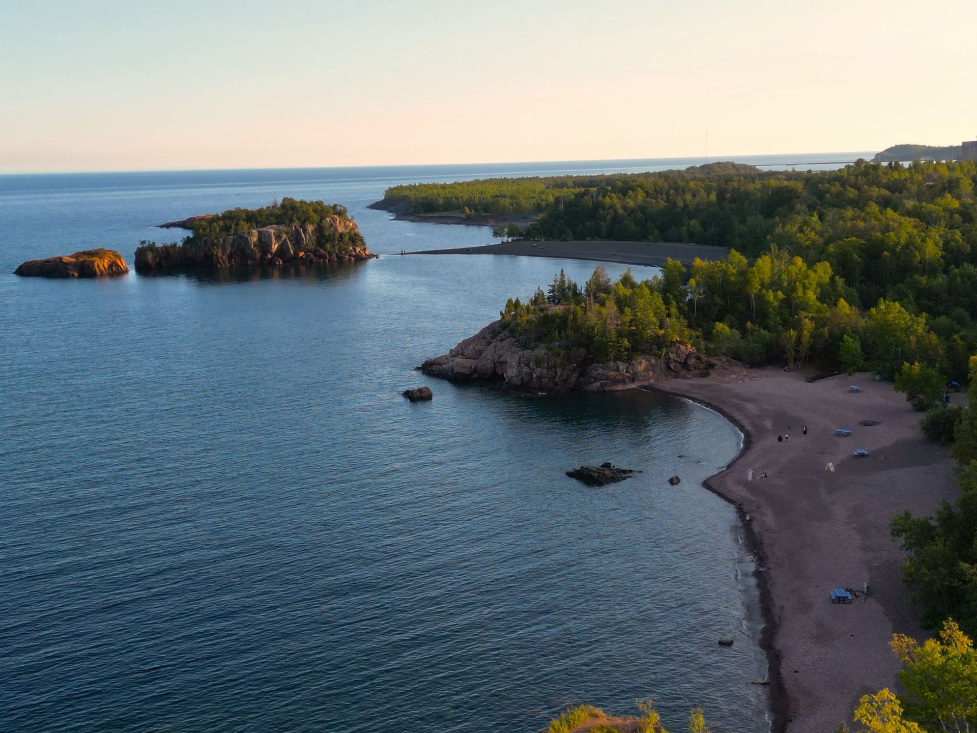 Coastal view: blue water, small islands, tree-covered cliffs, beach, and a clear sky.
