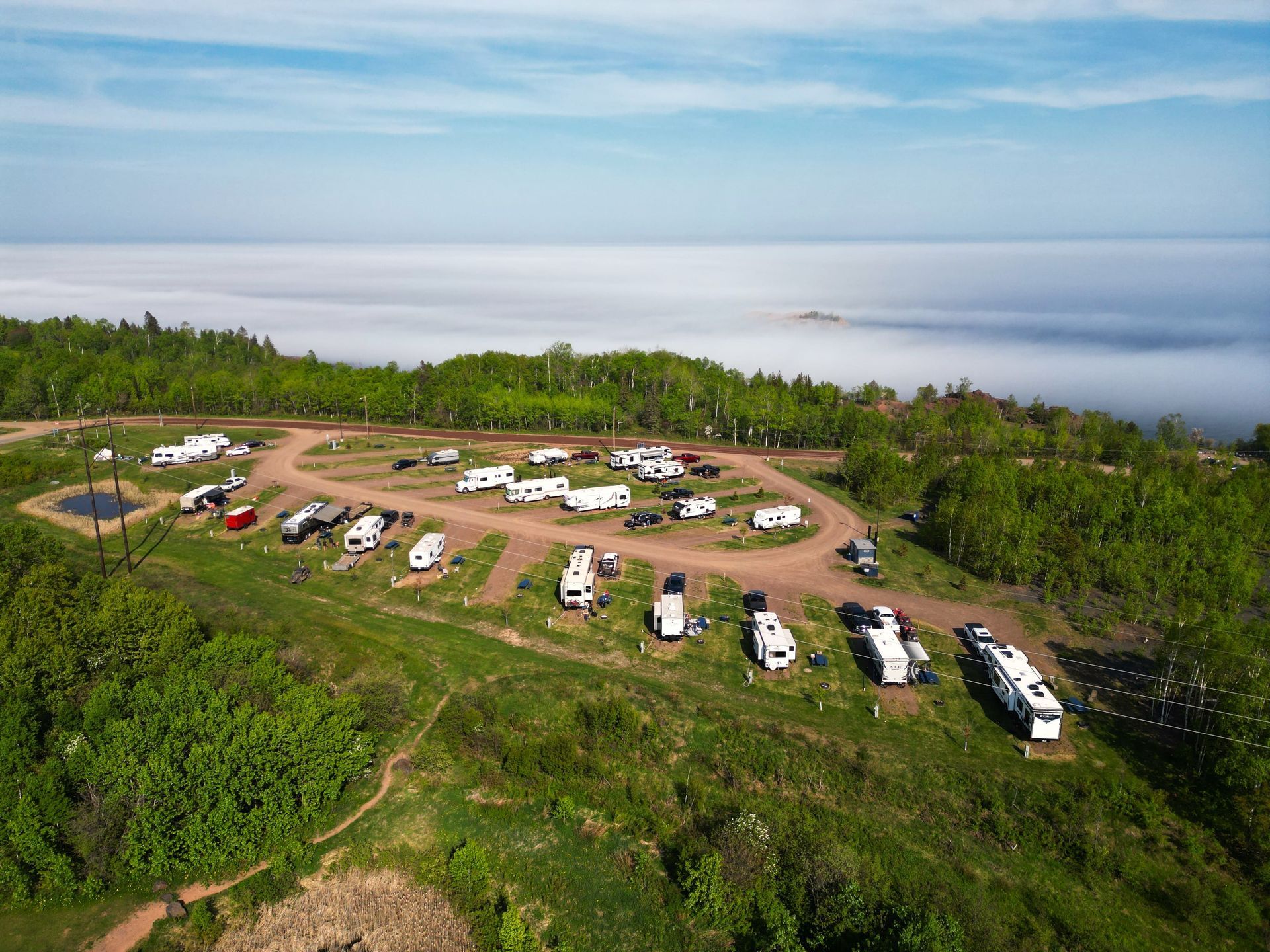 Campground with RVs overlooking a sea of fog, on a hillside with green grass and trees.