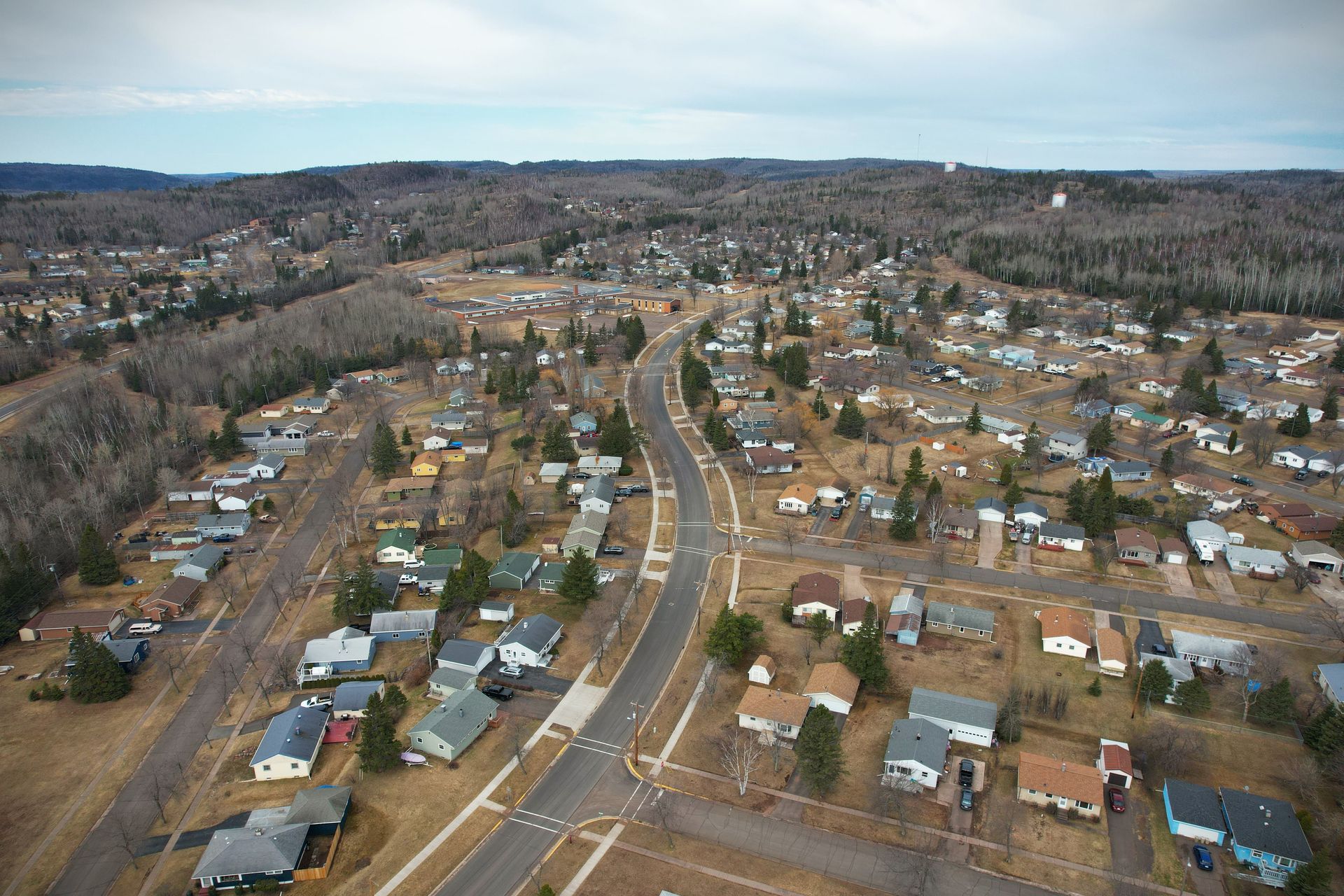 Aerial view of a small town with houses along a winding road, surrounded by bare trees and hills.