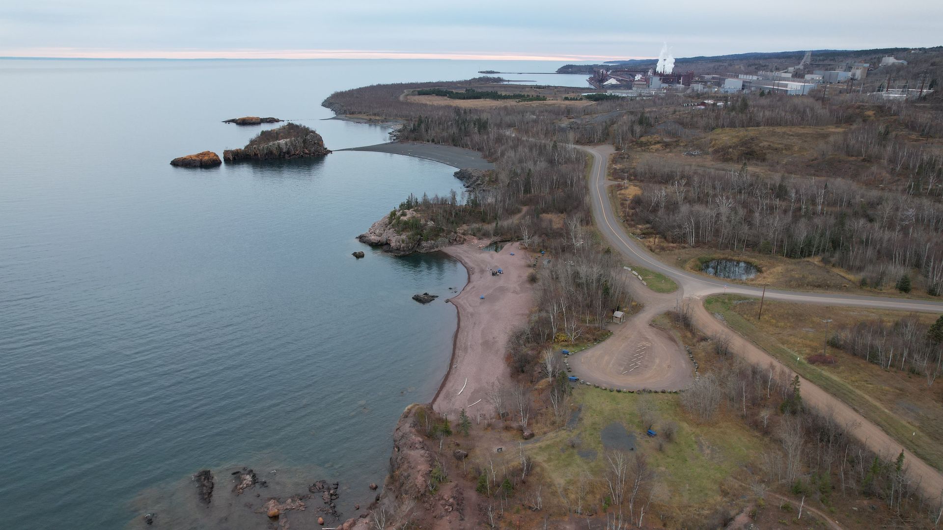 Coastal landscape with a rocky shoreline, water, and sparse trees under a cloudy sky.