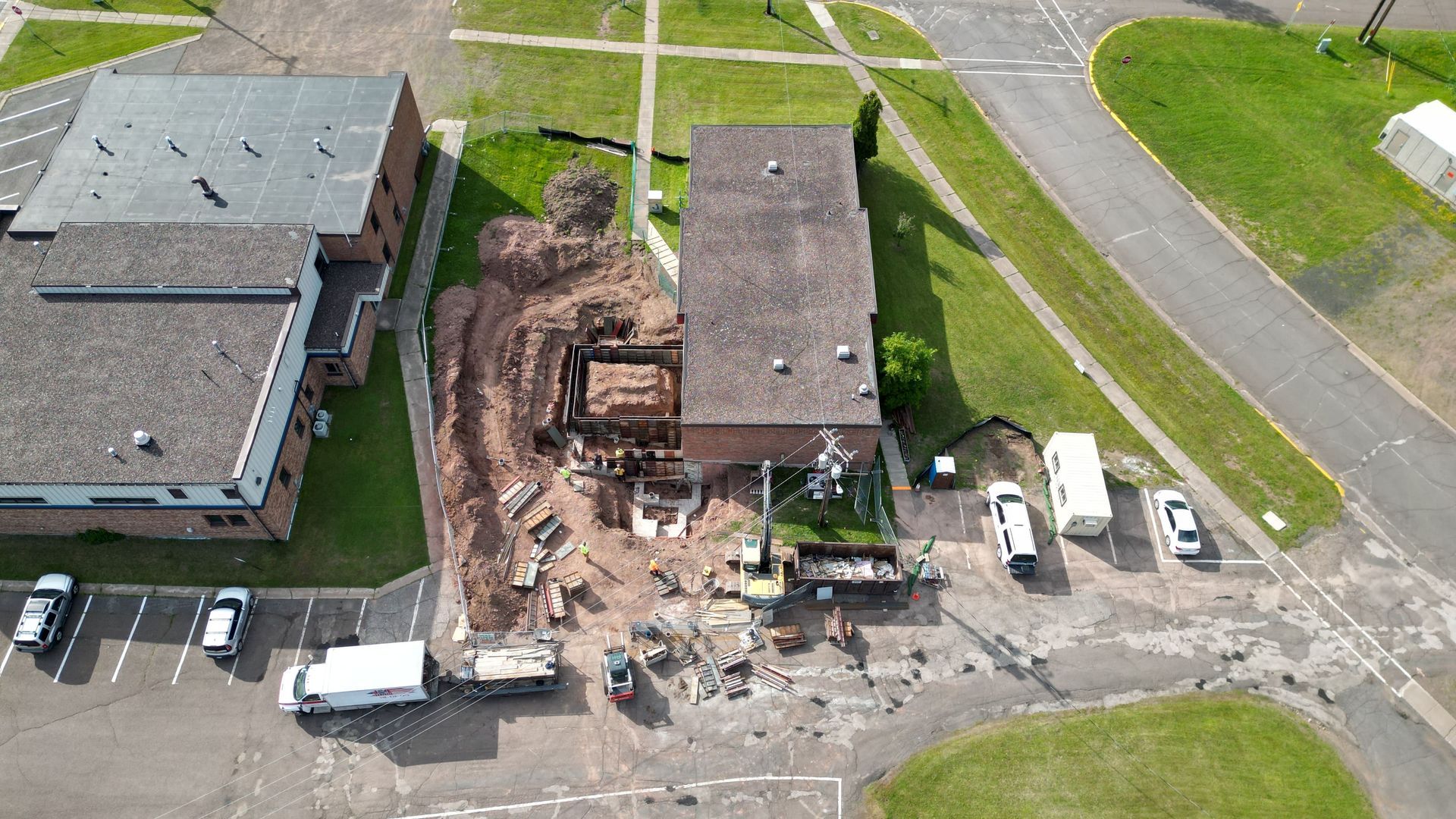 Aerial view of building construction site, with excavation equipment and vehicles surrounding the building.