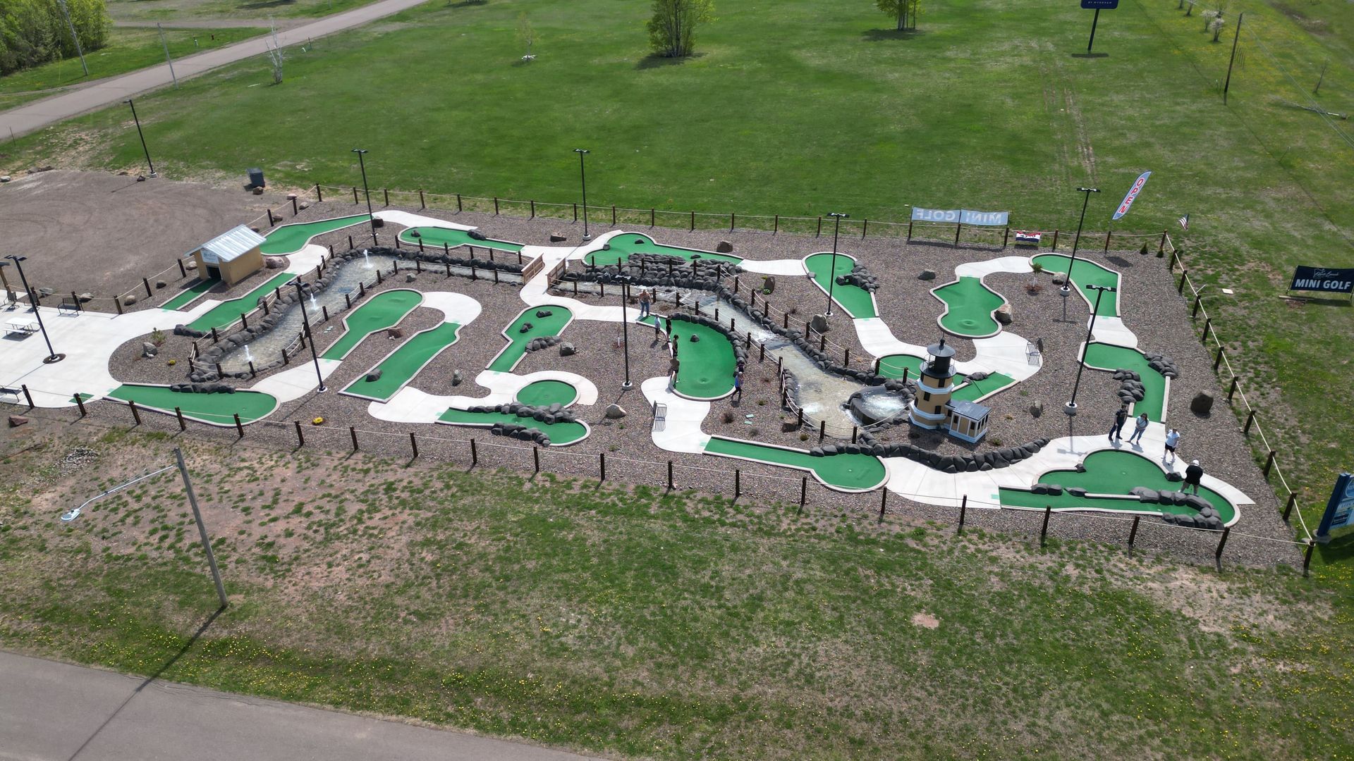 Aerial view of a miniature golf course with green turf, winding paths, and a water feature.