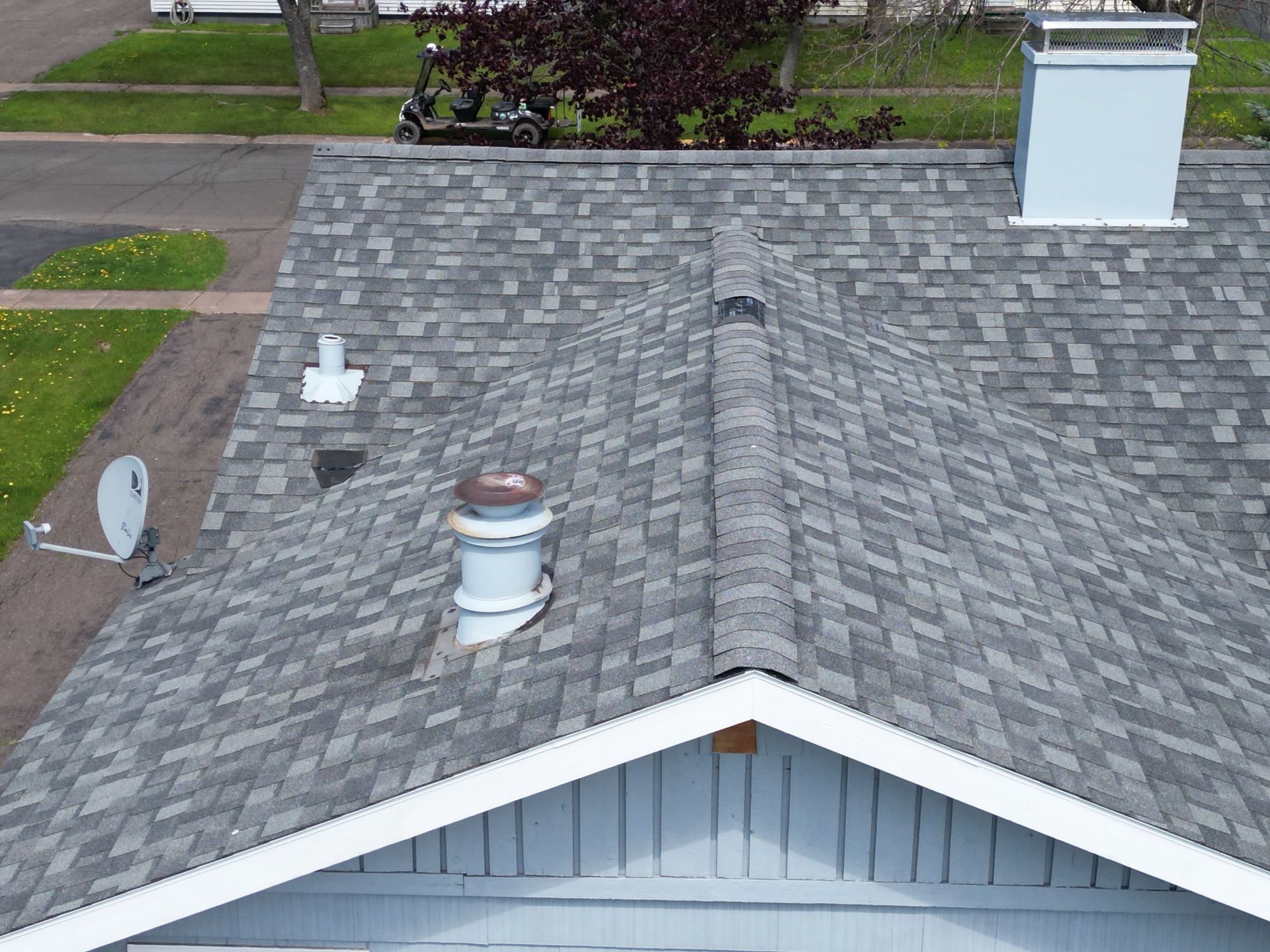 Gray shingle roof of a house with chimneys, vents, and a satellite dish.