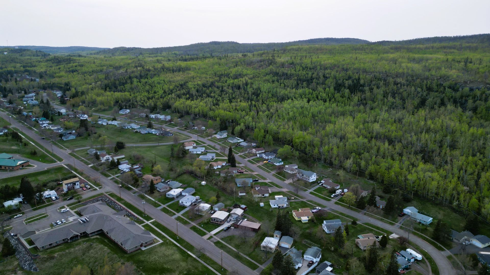 Aerial view of a small town nestled by a lush green forest, with houses lining a road.