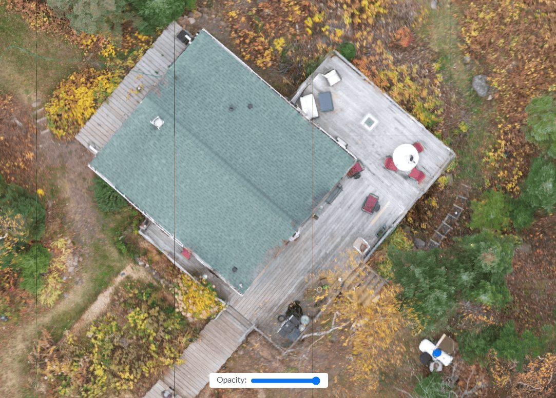 Overhead view of a cabin with a green roof, two decks, and a surrounding forest during autumn.