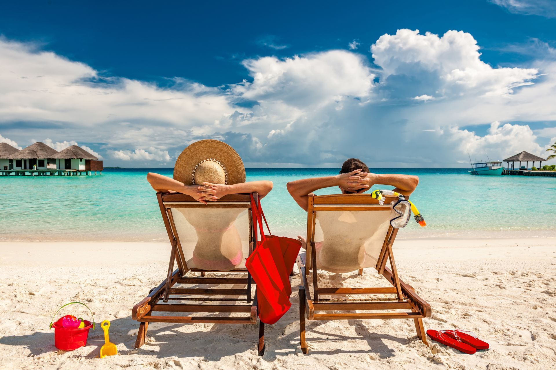 a man and a woman are sitting in beach chairs on the beach holding hands .