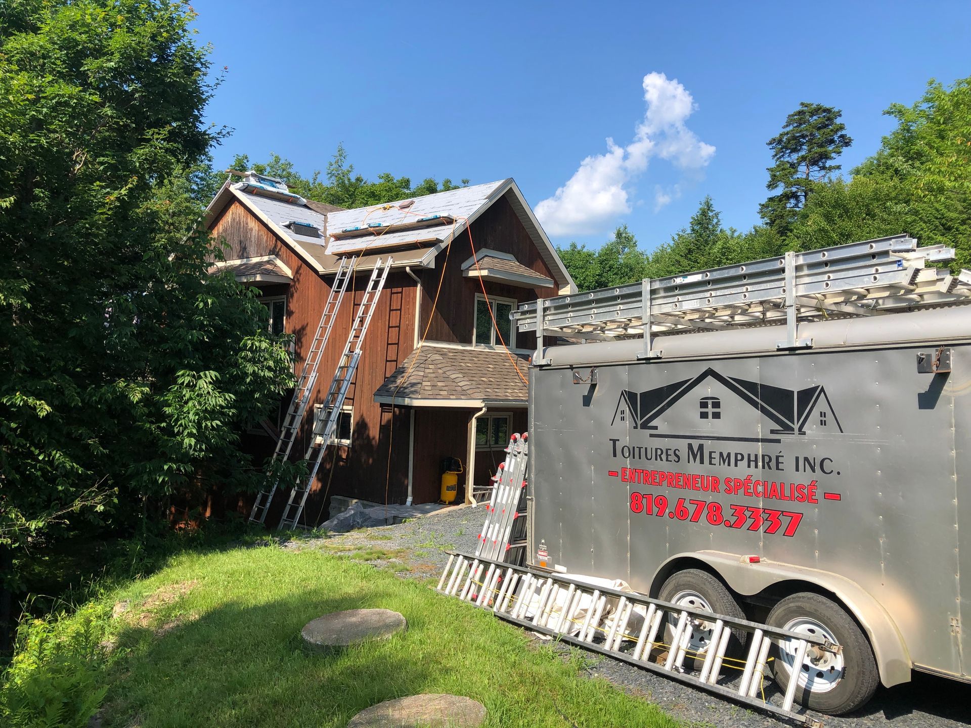 Une remorque avec une échelle à l'arrière est garée devant une maison.