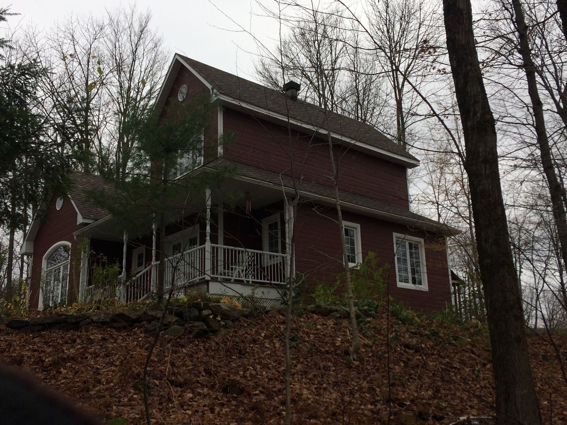 Une maison rouge avec un porche est assise au sommet d'une colline entourée d'arbres.