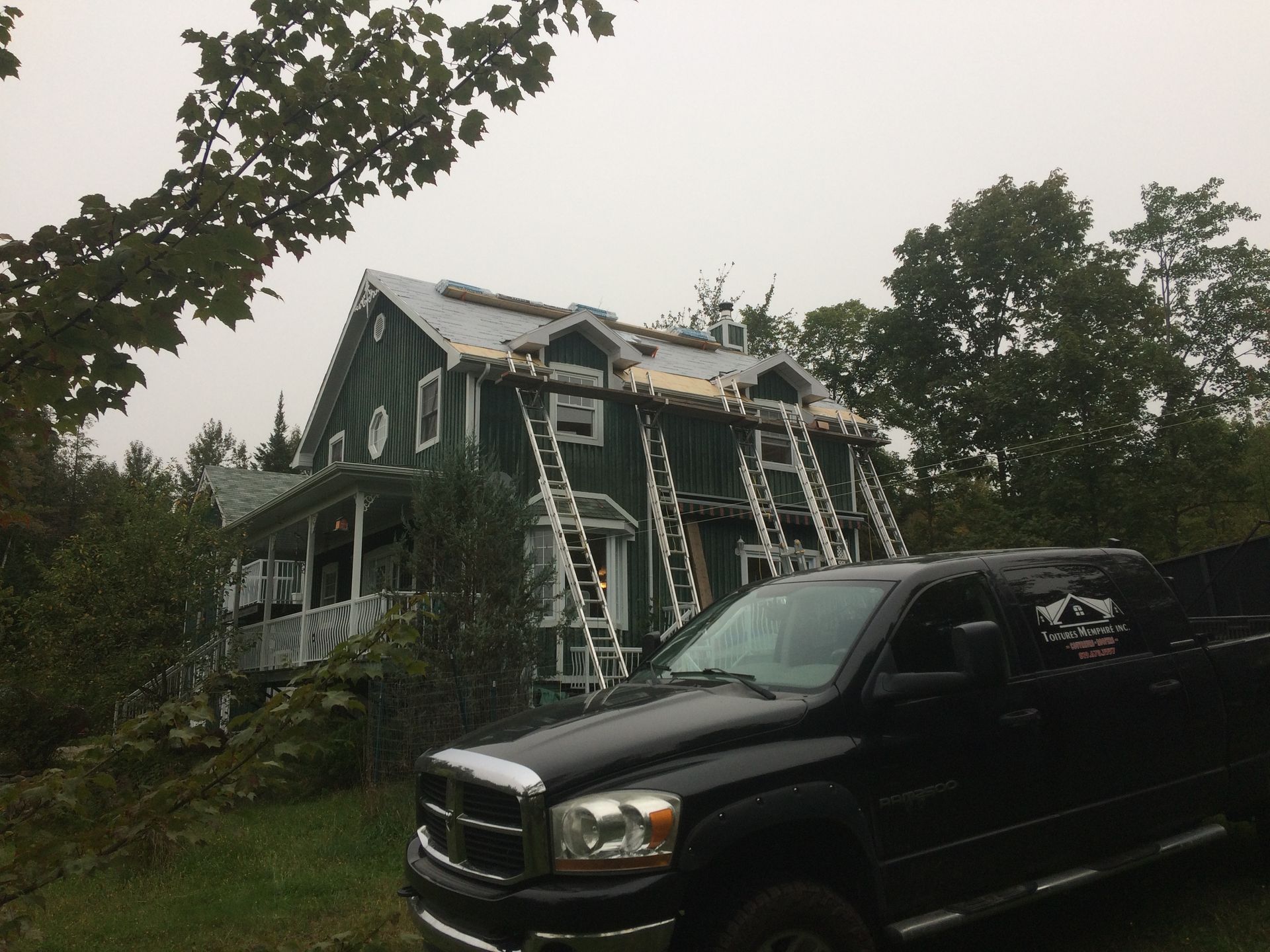 Un camion noir est garé devant une maison verte.