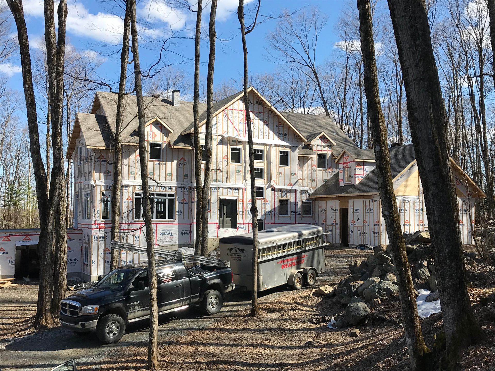 Une grande maison est en construction dans les bois et un camion est garé devant.