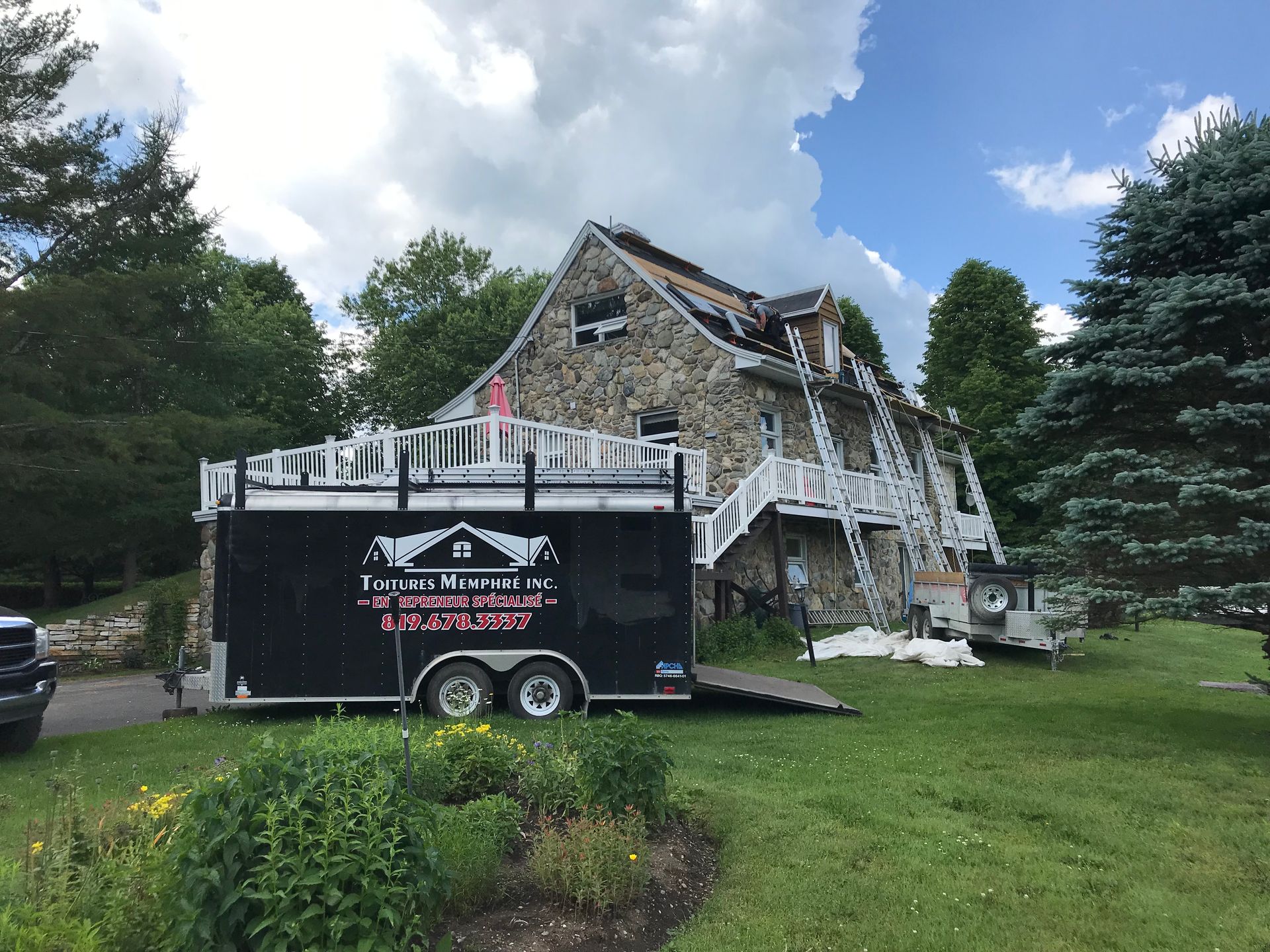 Une remorque noire est garée devant une grande maison.