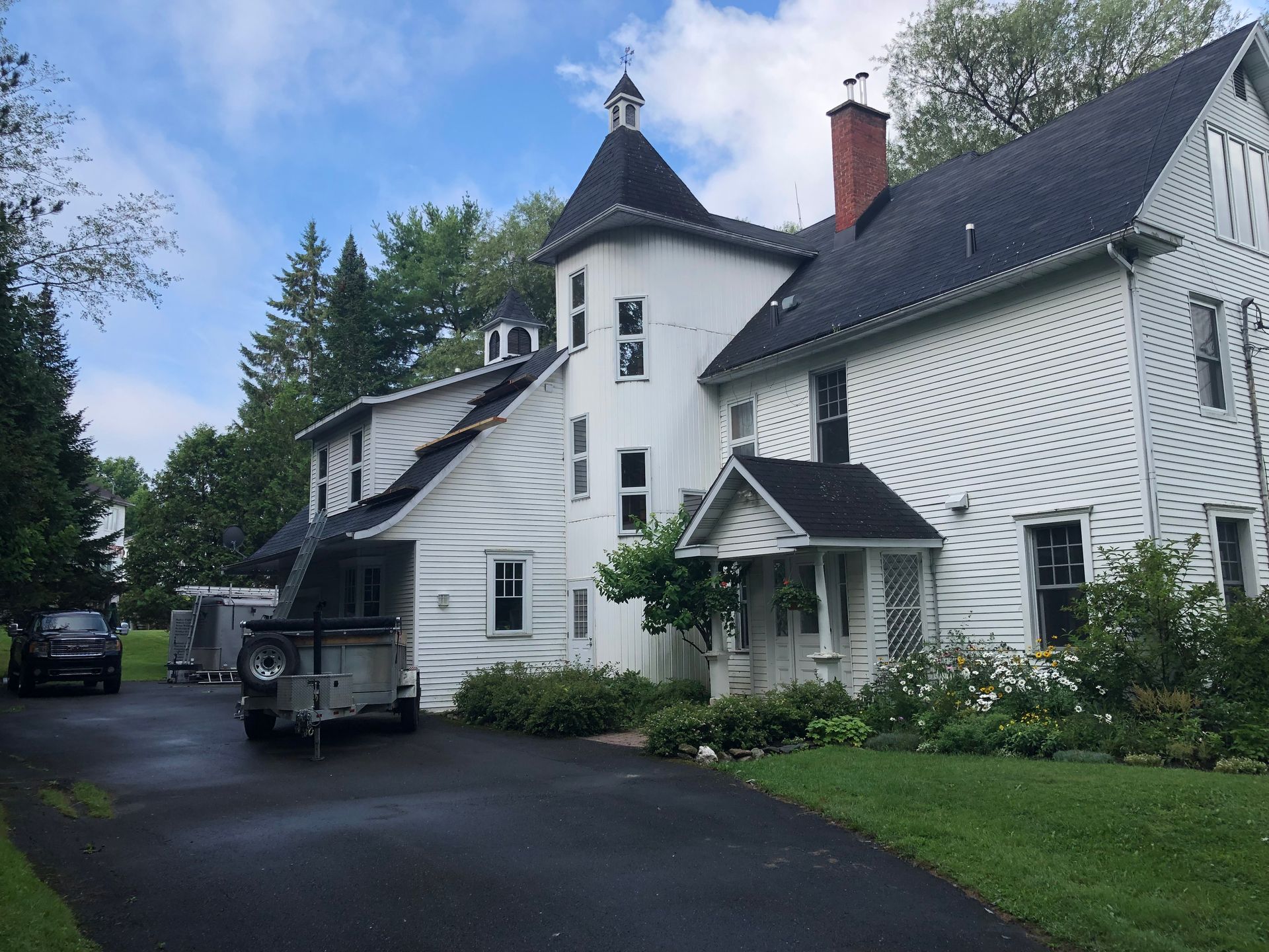 Une grande maison blanche avec un toit noir et une caravane garée devant.