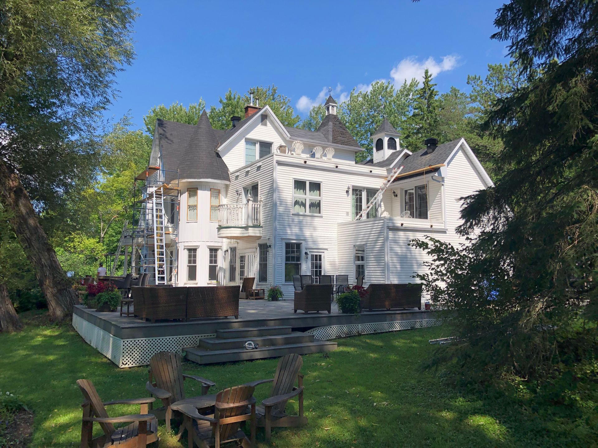 Une grande maison blanche avec une terrasse et des chaises devant.