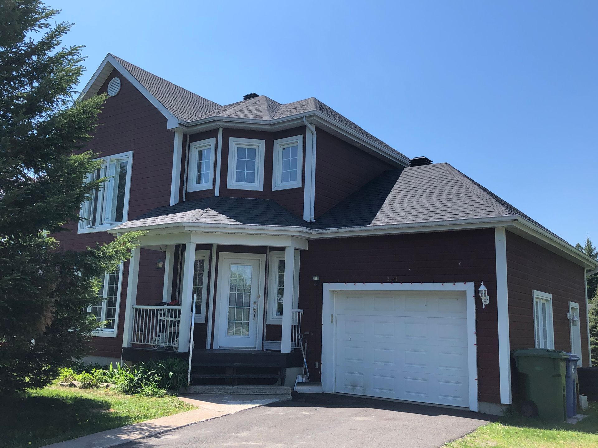 Une grande maison rouge avec une porte de garage blanche et un ciel bleu en arrière-plan.