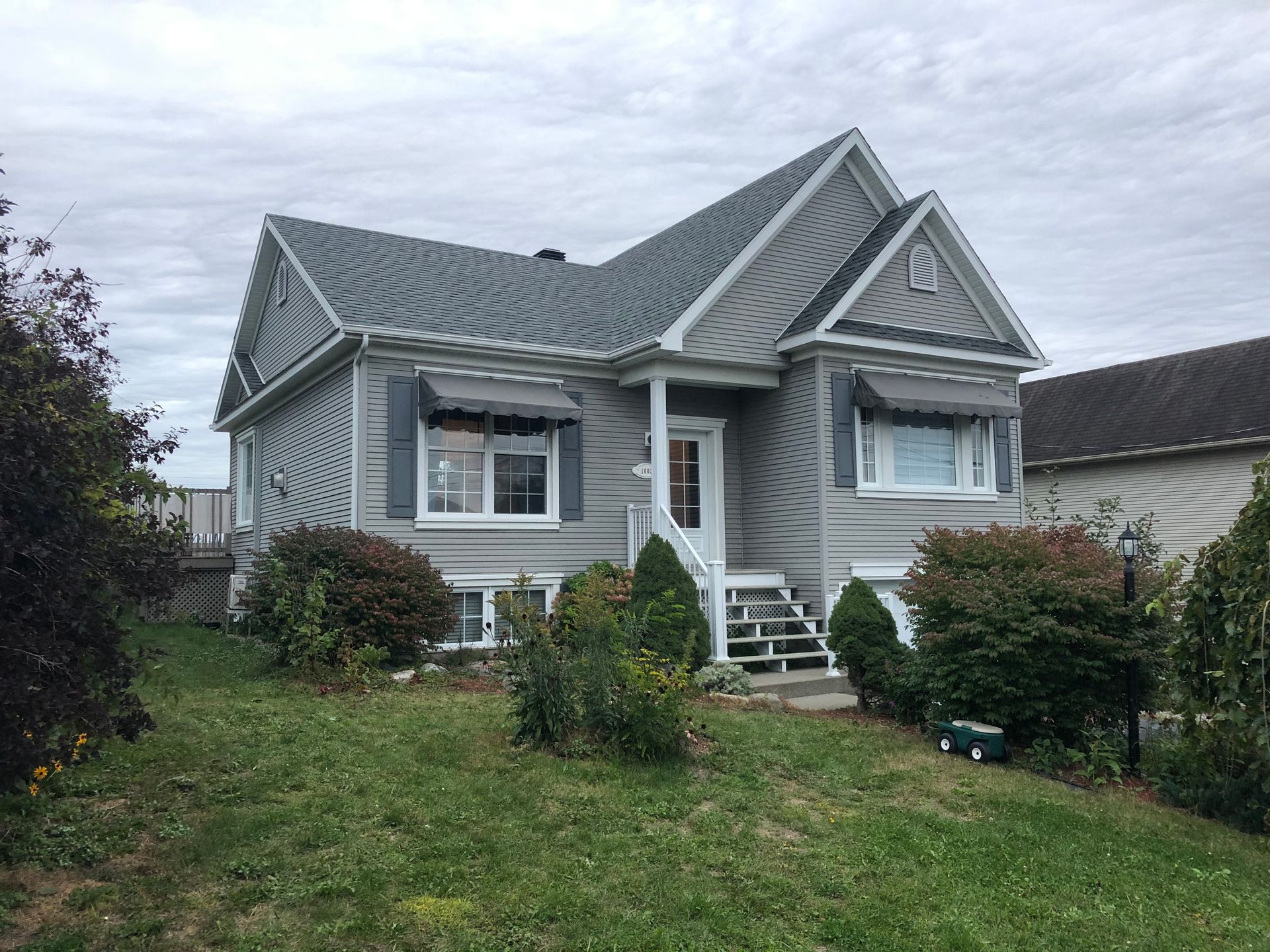 Une petite maison au toit gris est assise au sommet d'une colline herbeuse.