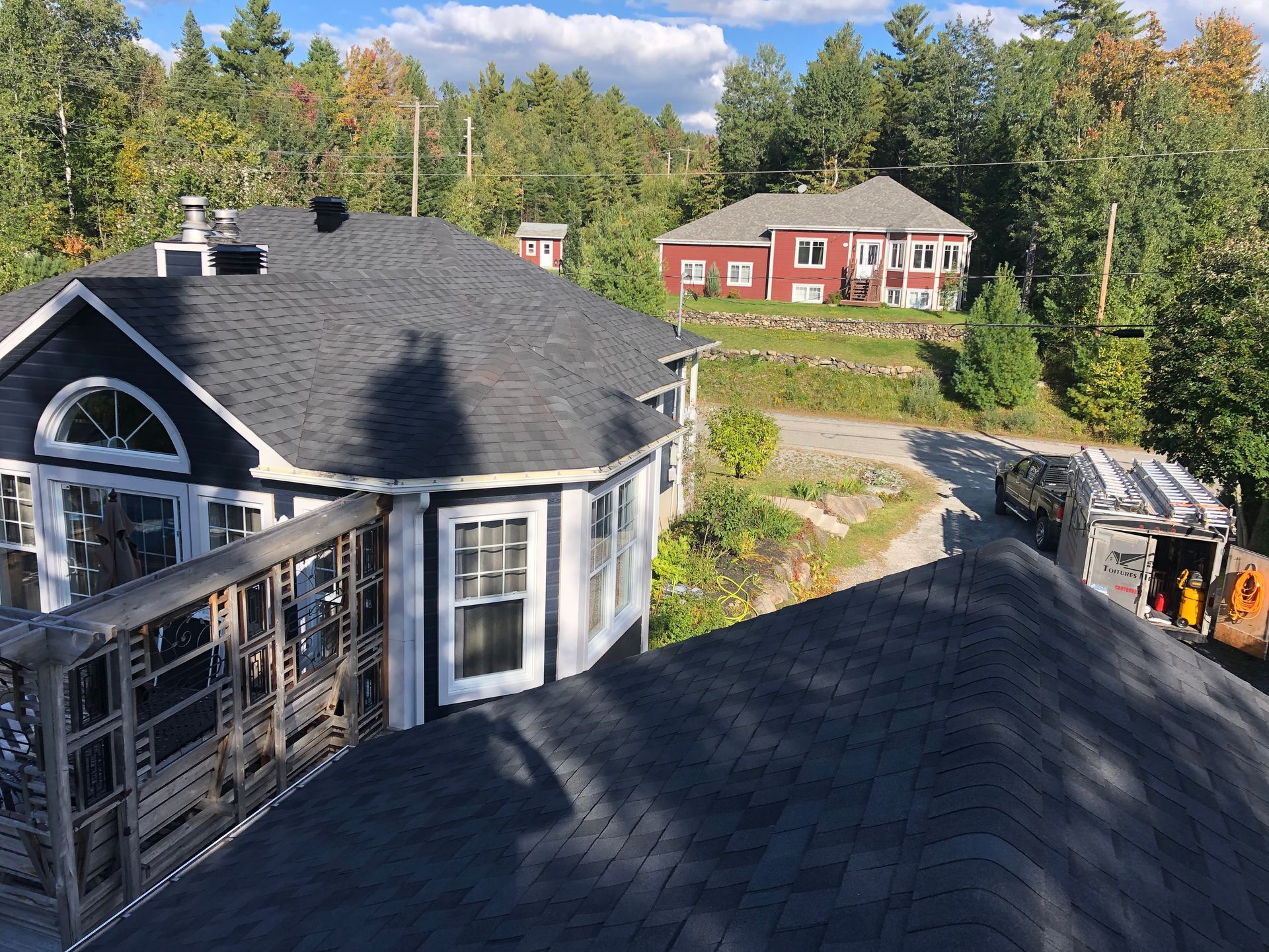 Une grande maison avec un toit noir et une maison rouge en arrière-plan.