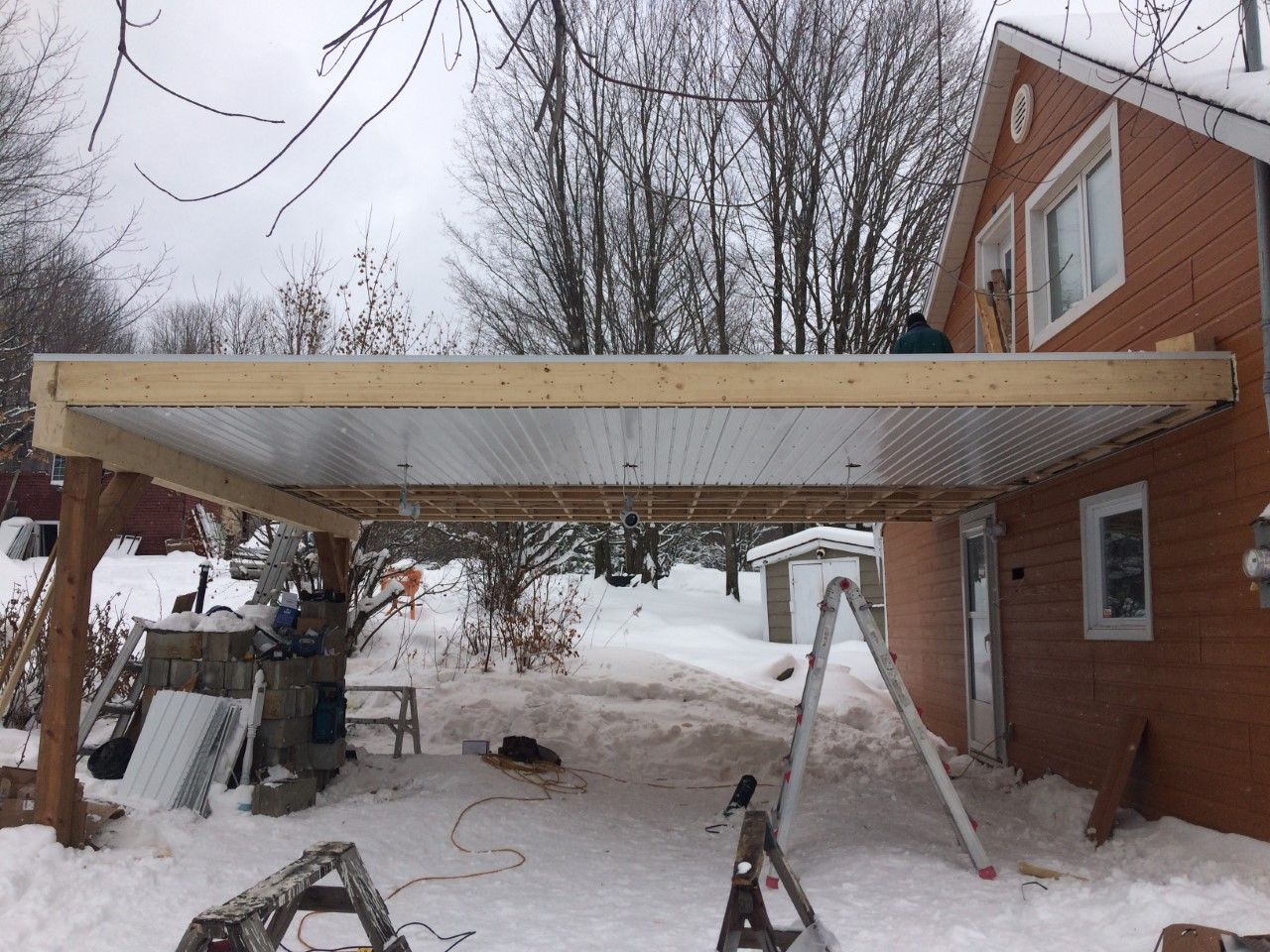 Un abri pour voiture est en cours de construction sous une maison en briques sous la neige.