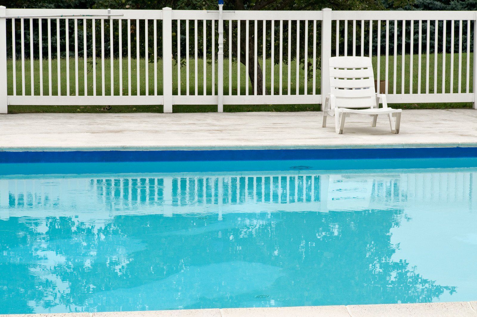 Swimming pool with white fence and chair; reflections in water.
