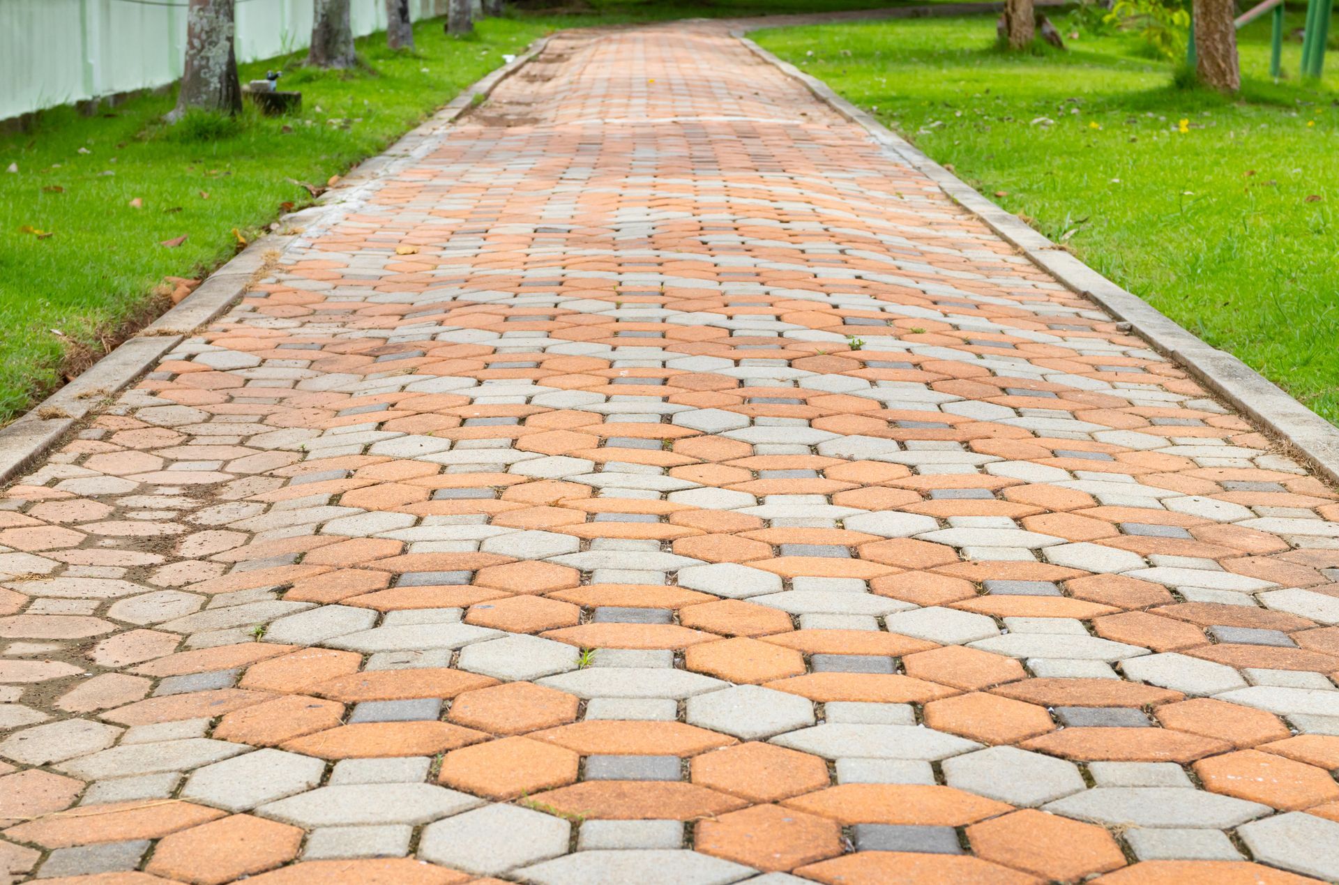 A brick walkway leading to a grassy area in a park.