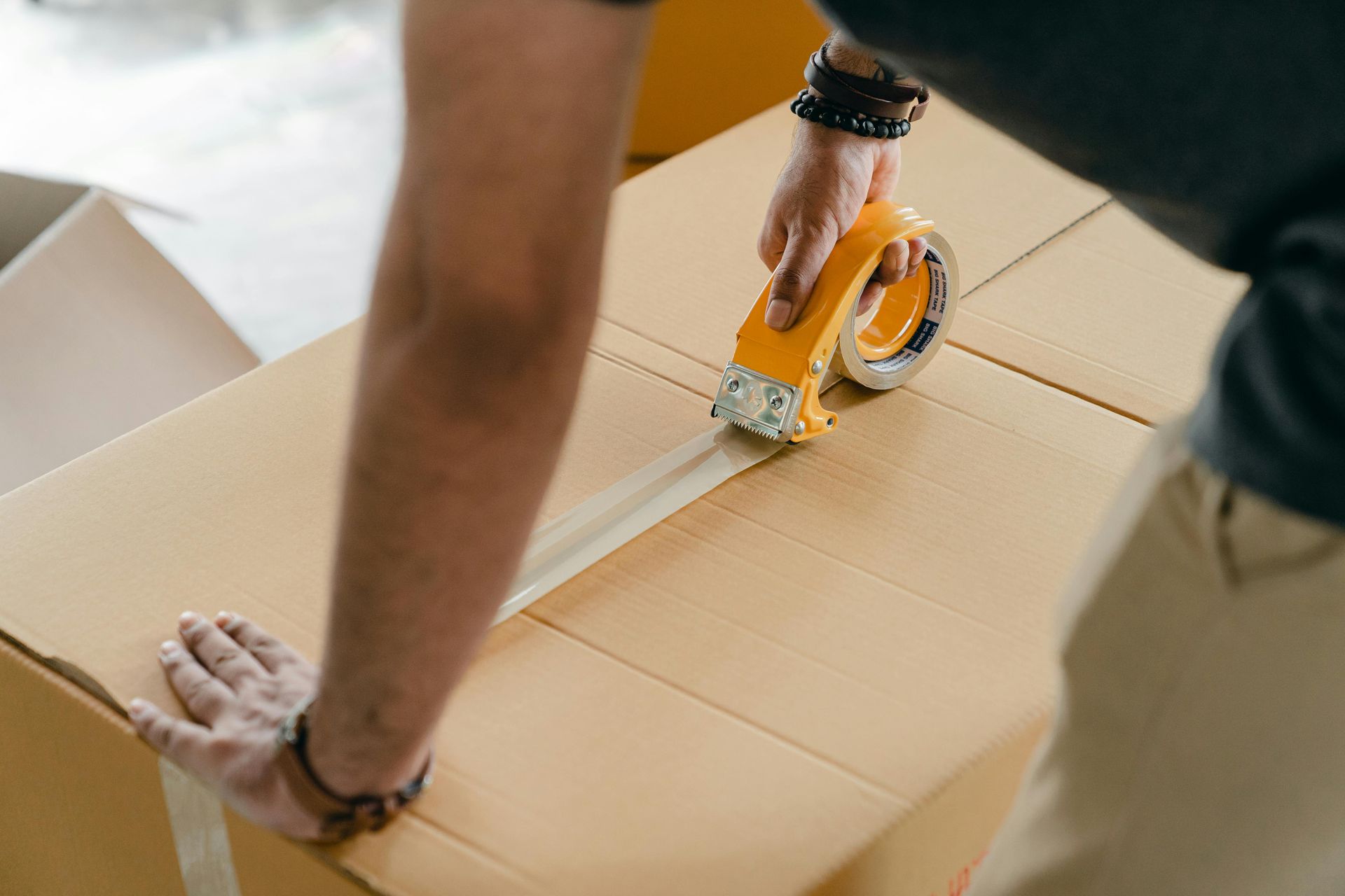 Person taping up a cardboard box, holding the tape dispenser.