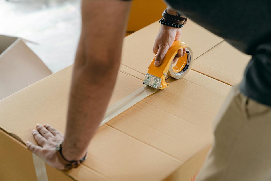 Person taping up a cardboard box, holding the tape dispenser.